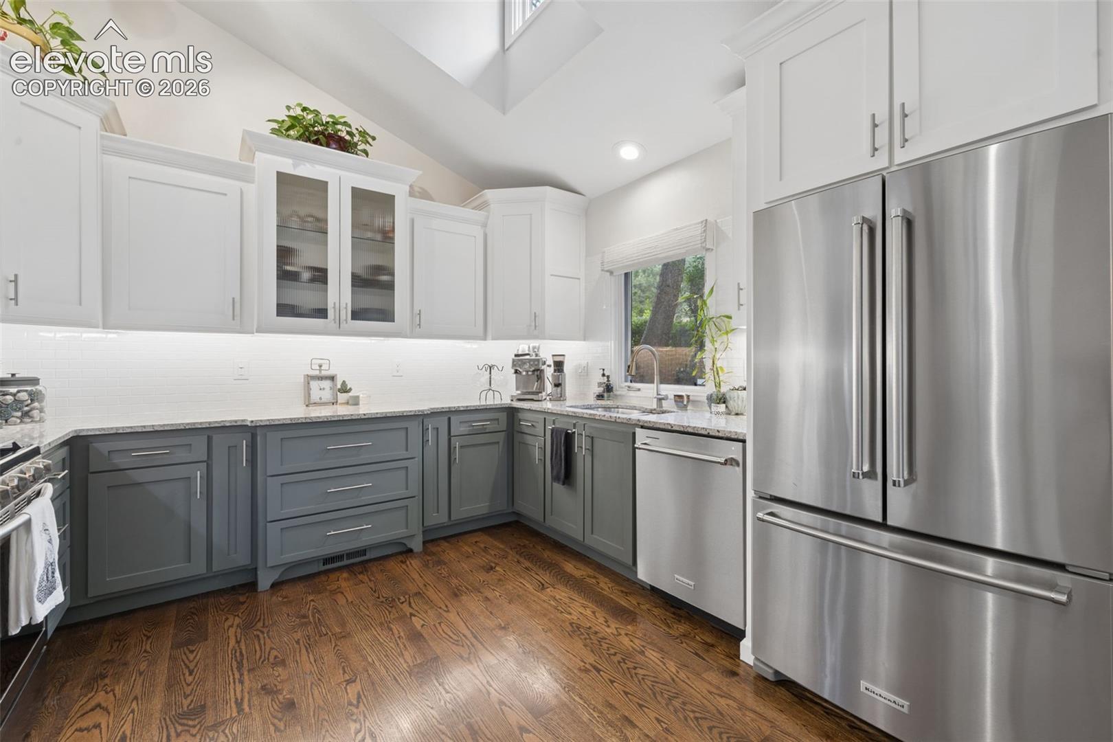 Kitchen with white and gray cabinets, stainless steel appliances, and warm wood flooring.