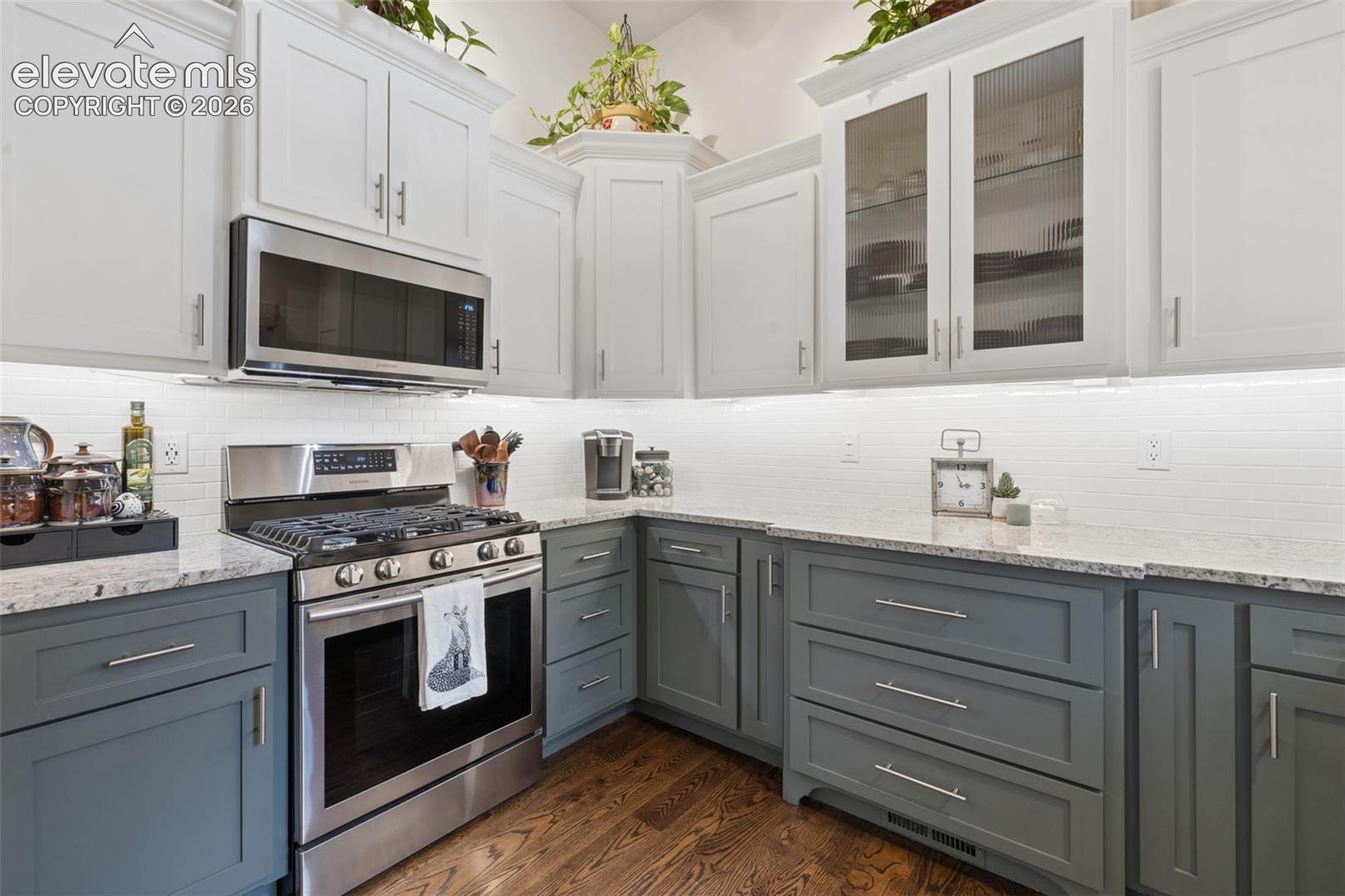 Kitchen with white upper cabinets, gray lower cabinets, stone counters, and a stainless steel range.