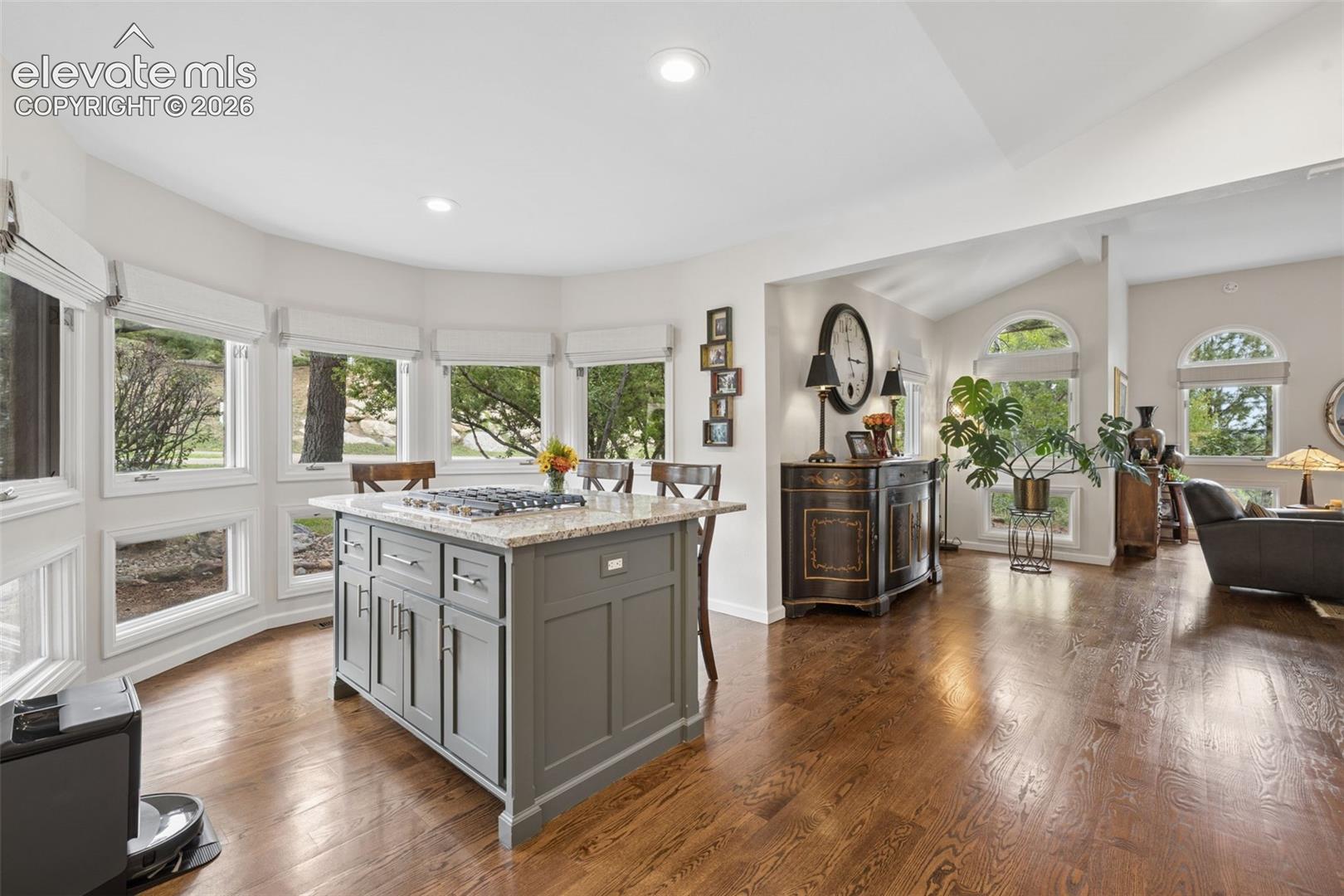 Kitchen with a gray granite-topped island, hardwood floors, and large windows opening to a living area.
