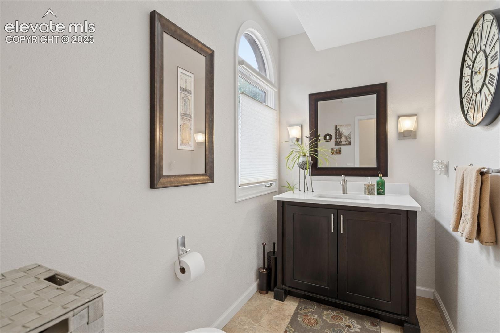 Bathroom vanity with dark wood cabinetry, a large mirror, and an arched window.