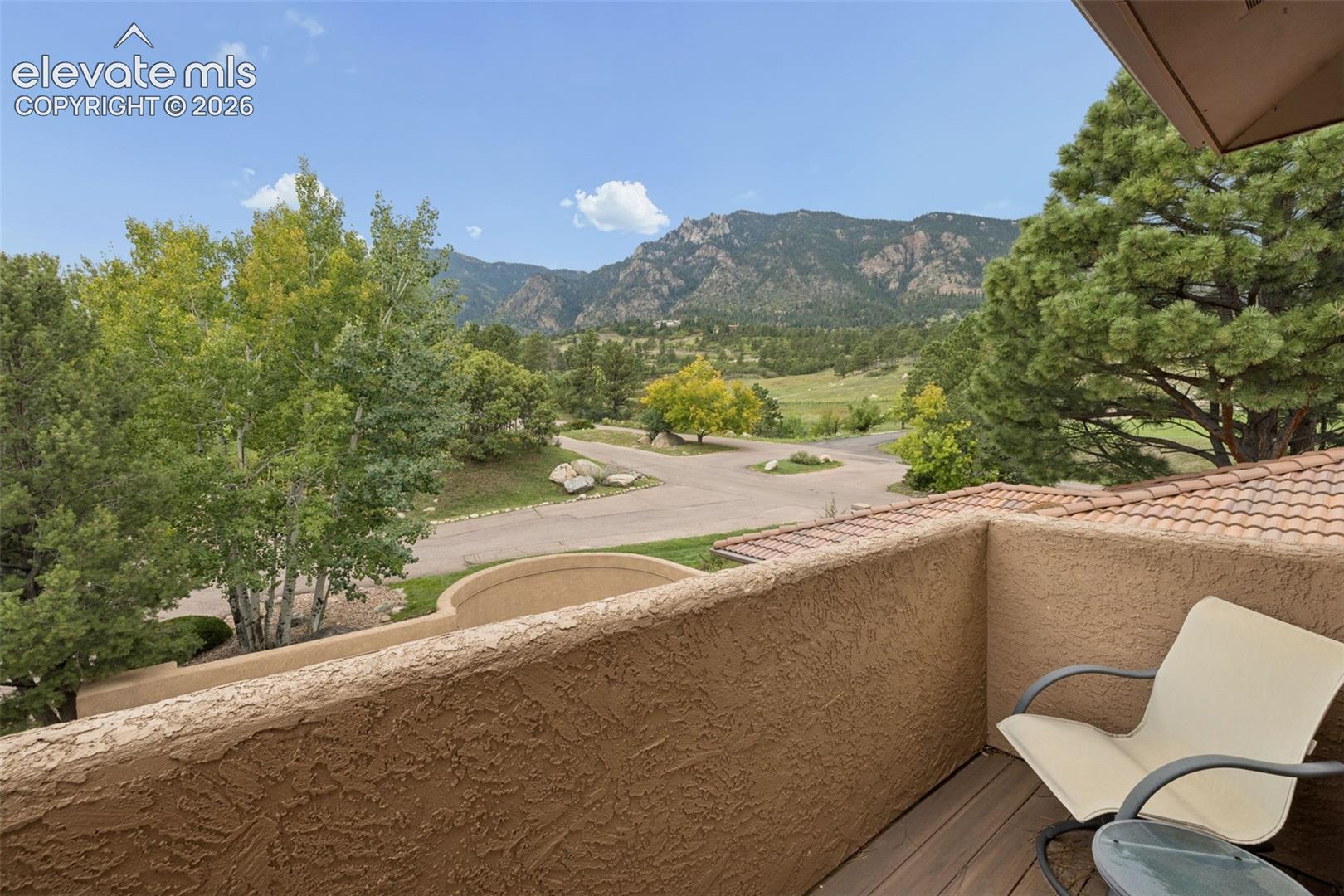 Balcony overlooking a tree-lined road and Rocky Mountain foothills, with a white chair in the foreground.
