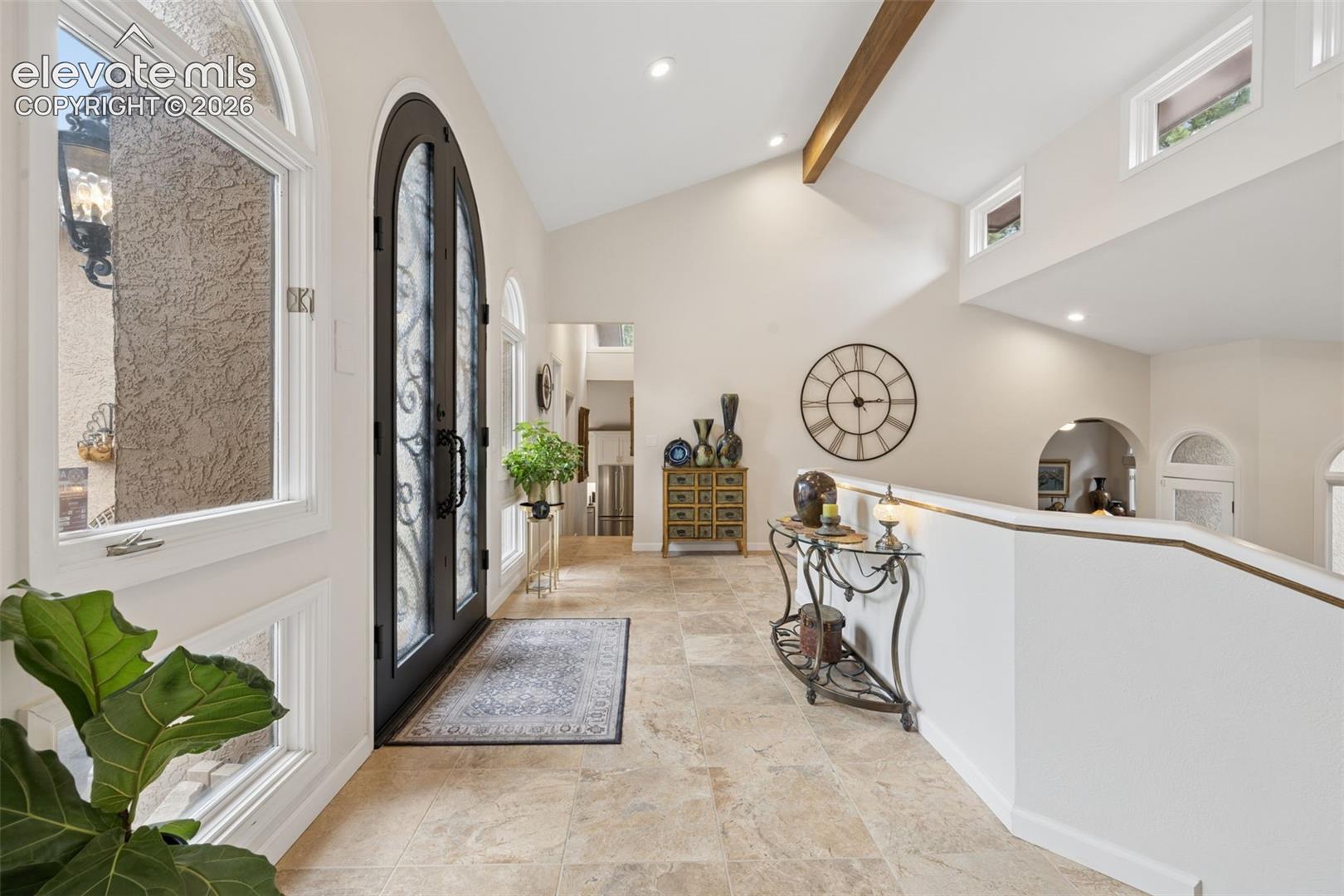 Entry foyer with arched black front door, tiled floor, and vaulted ceiling with exposed beam.