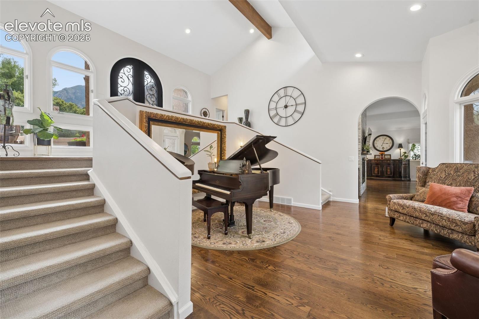 Entry hall with a carpeted staircase, grand piano, arched windows, and mountain views.