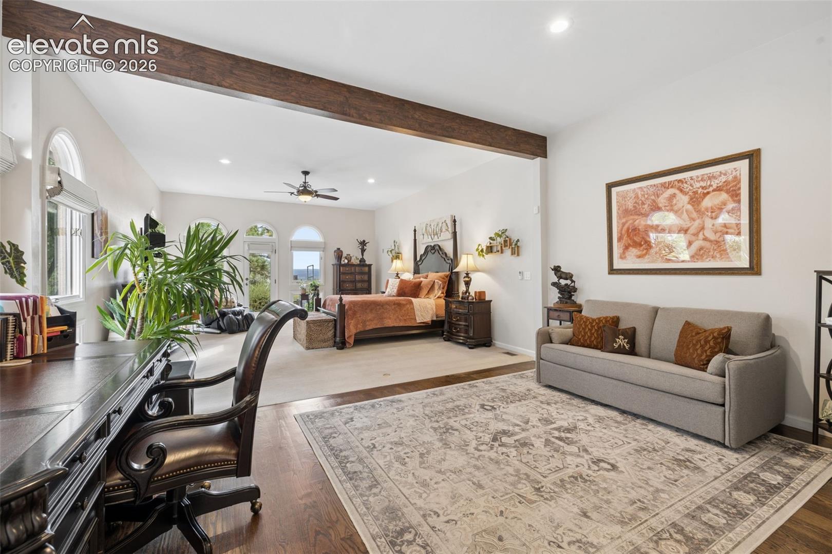Furnished bedroom with a four-poster bed, arched windows, and a gray sofa sitting area.