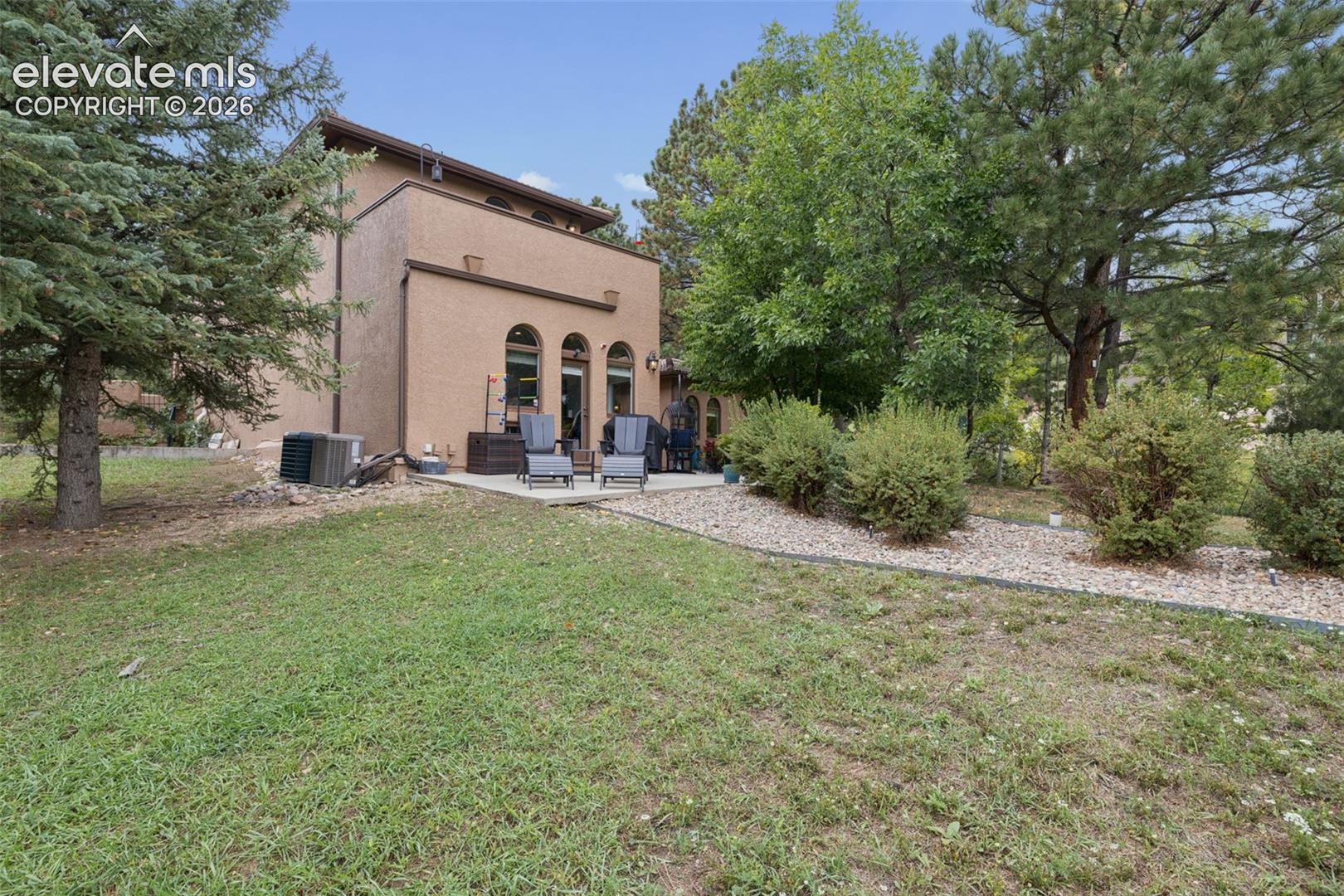 Rear of a tan stucco home with an arched-window patio, outdoor chairs, and a rock path through the lawn.