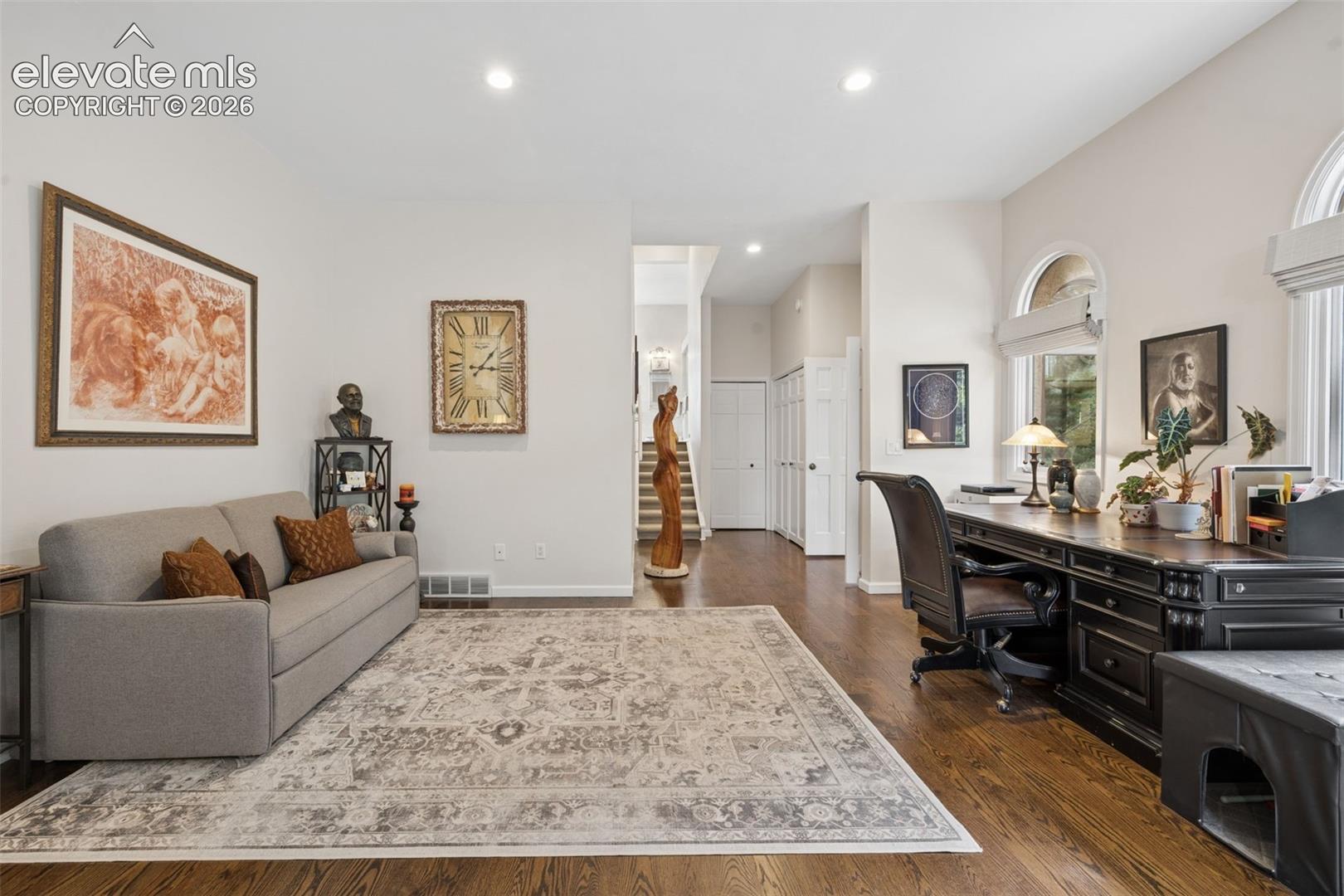 Living room and home office with a gray sofa, patterned rug, and dark wood desk.