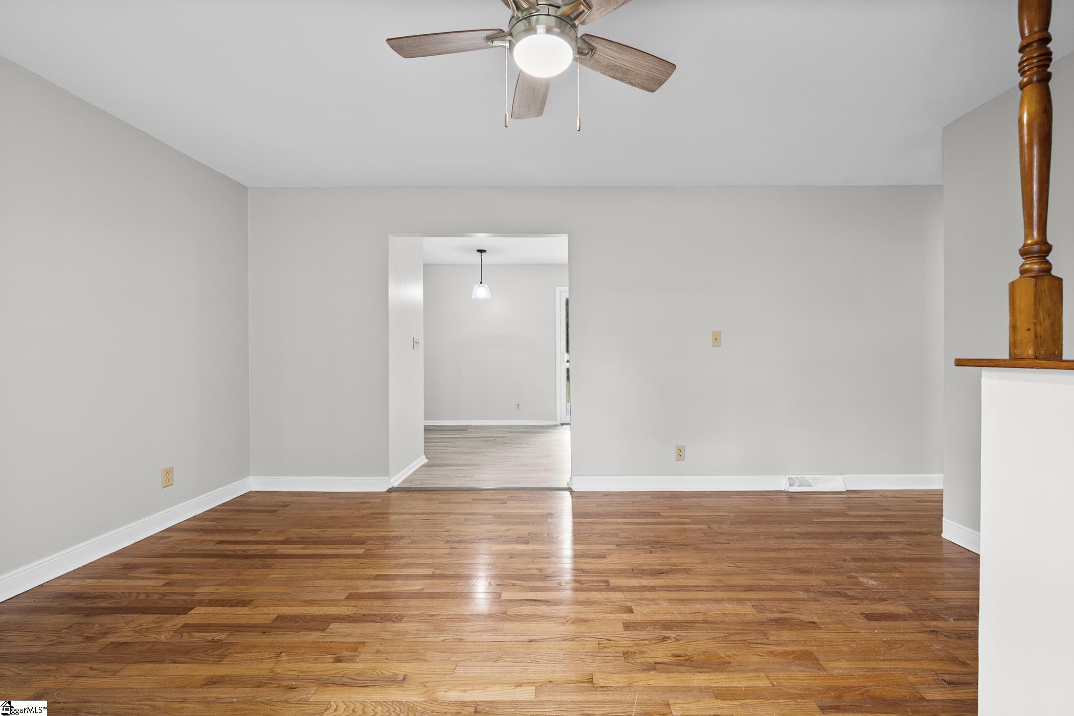 Vacant room with hardwood floors, a ceiling fan, and an open doorway to an adjoining room.
