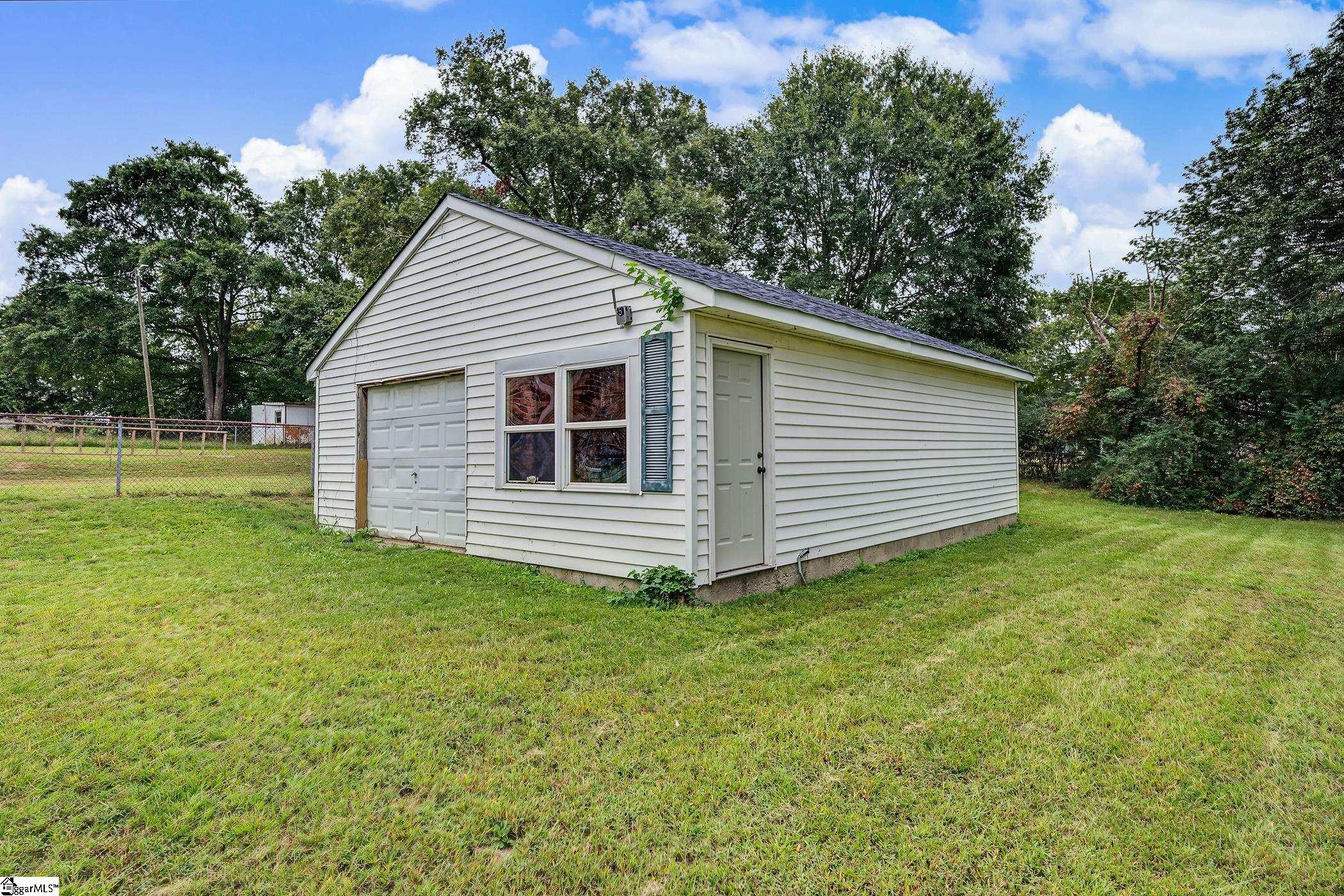 Detached white garage with an overhead door, four-pane window, and separate side entry in a grassy yard.