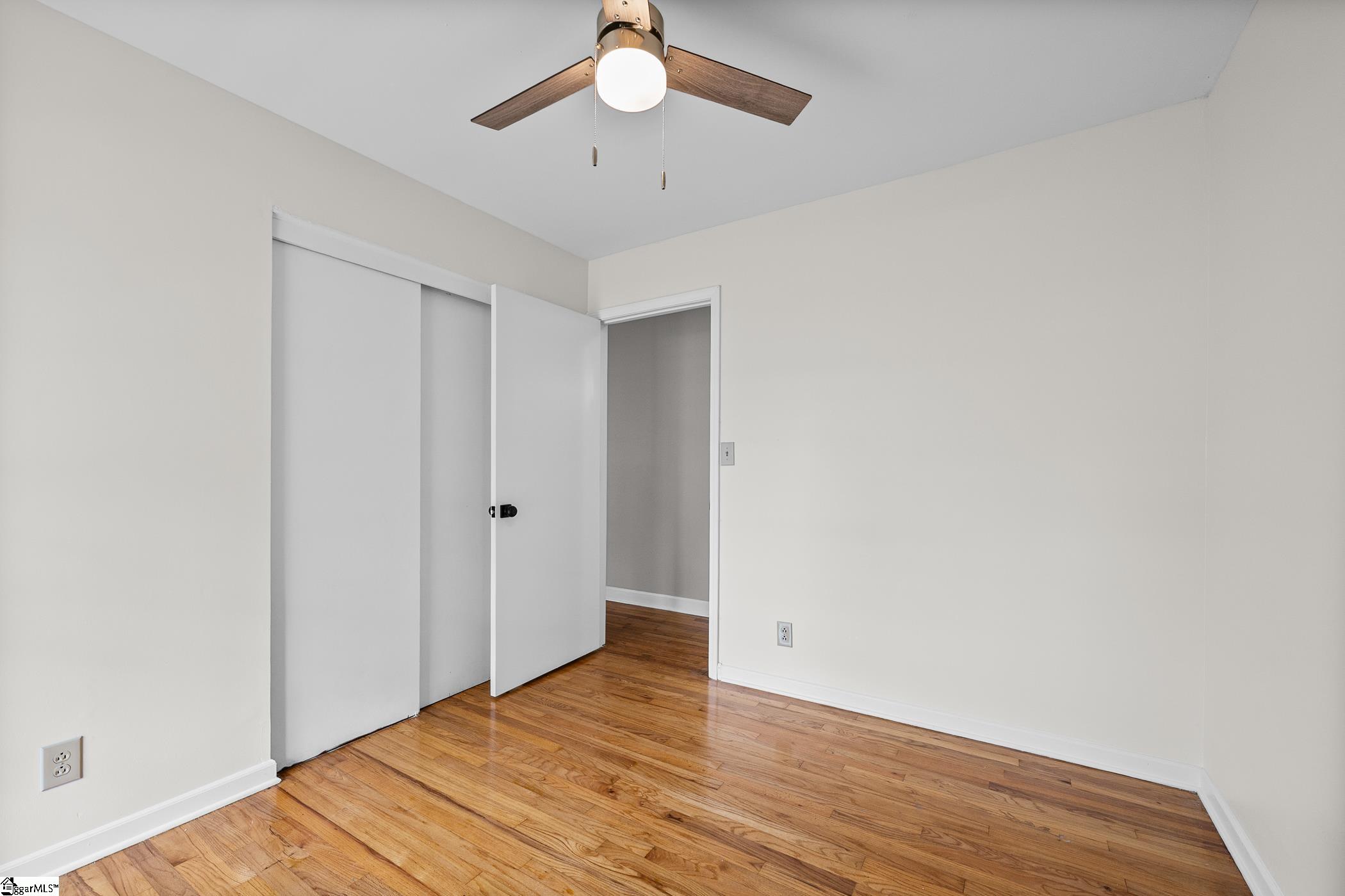 Empty room with hardwood floors, sliding closet doors, and a ceiling fan.