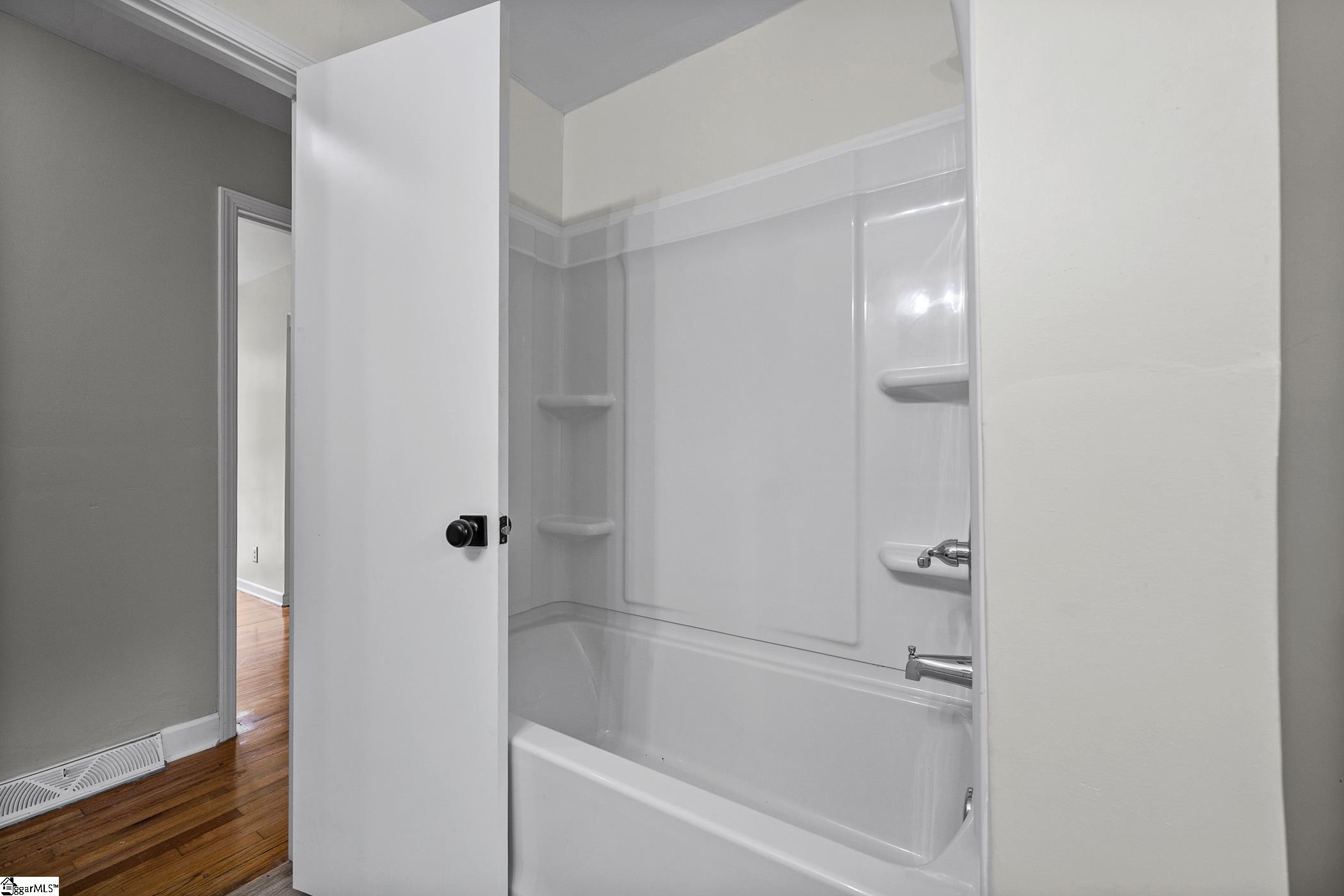 Bathroom tub and shower with built-in corner shelves and chrome fixtures, viewed through an open door.