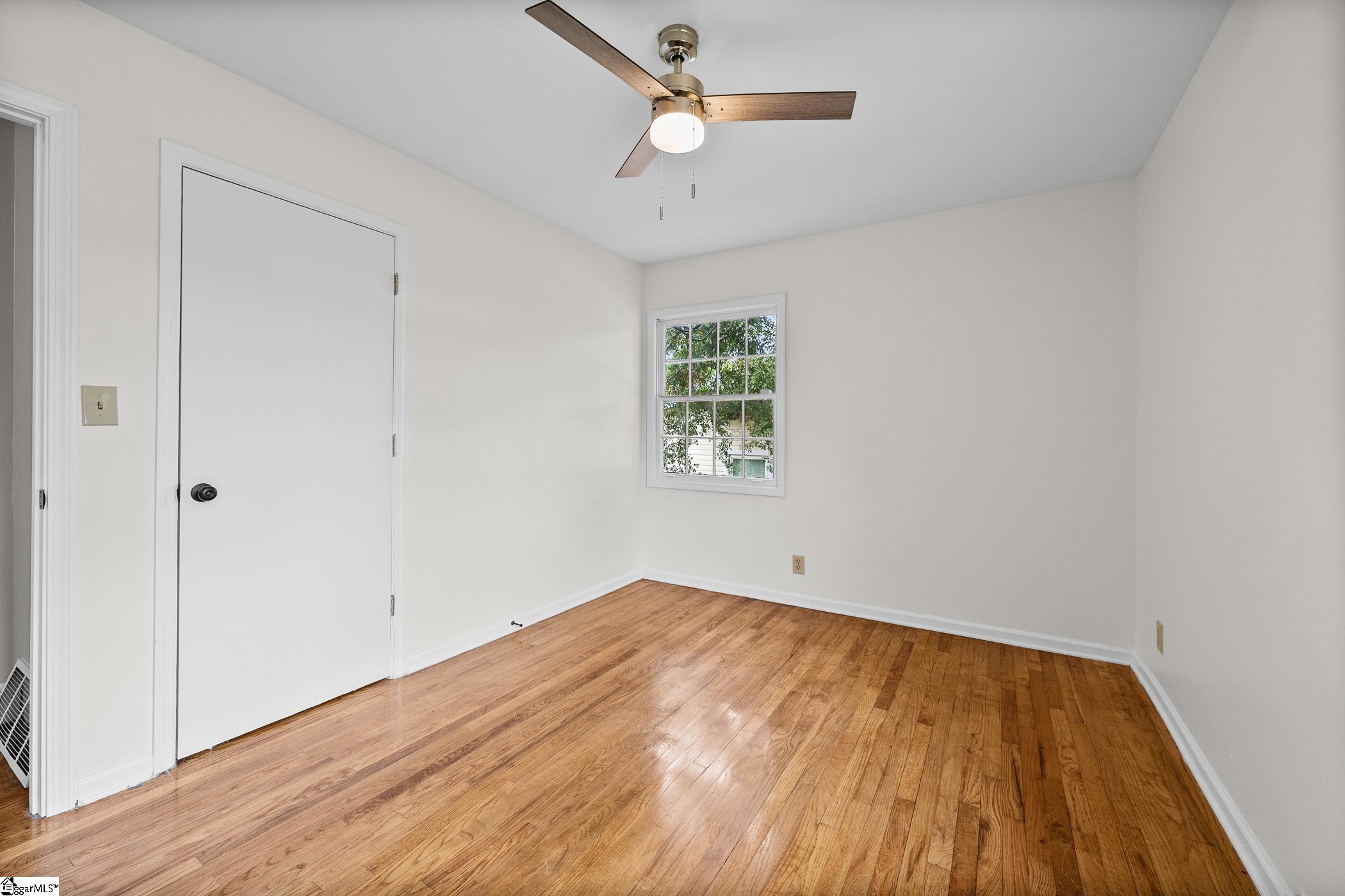 Empty room with hardwood floors, a ceiling fan, and a small divided-pane window.