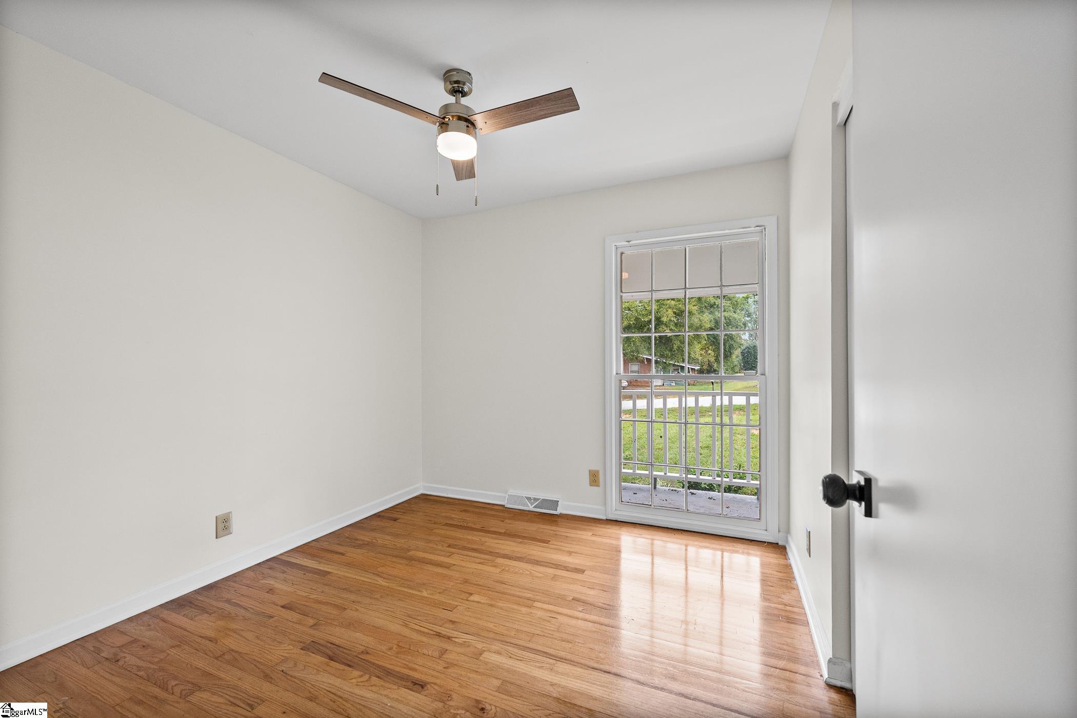 Empty room with polished hardwood floors, a ceiling fan, and a glass-paneled door to the porch.