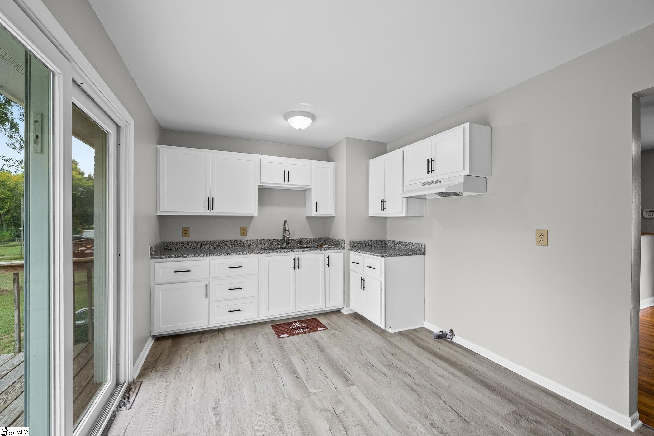 Vacant kitchen with white cabinets, speckled countertops, and a sliding glass door to the deck.