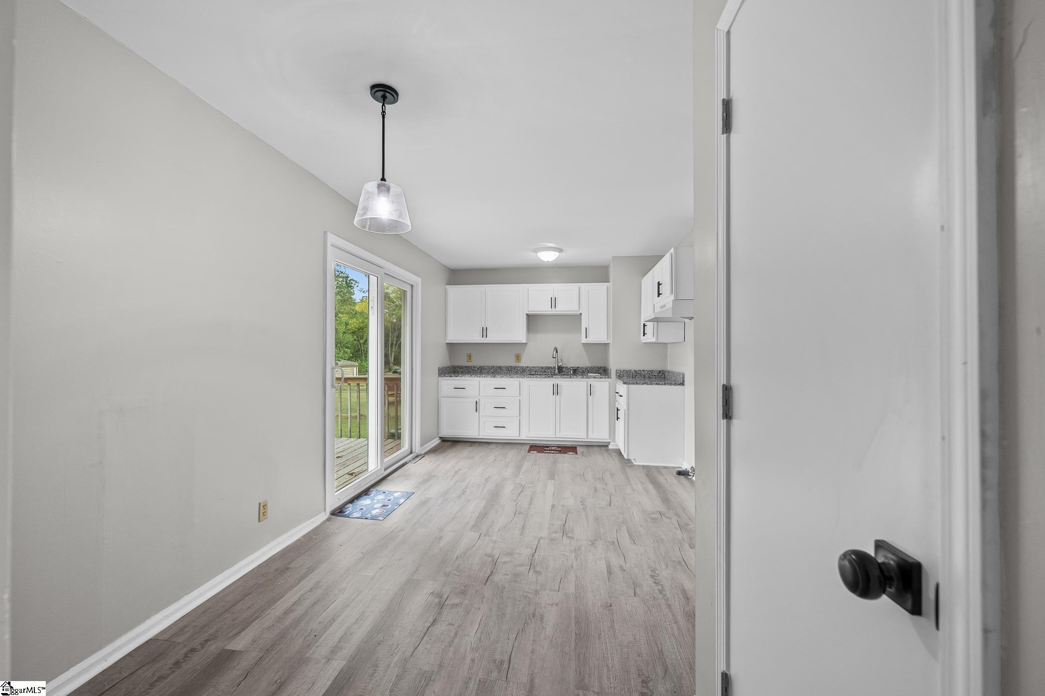 Empty kitchen with white cabinets, gray countertops, and sliding glass doors to a deck.