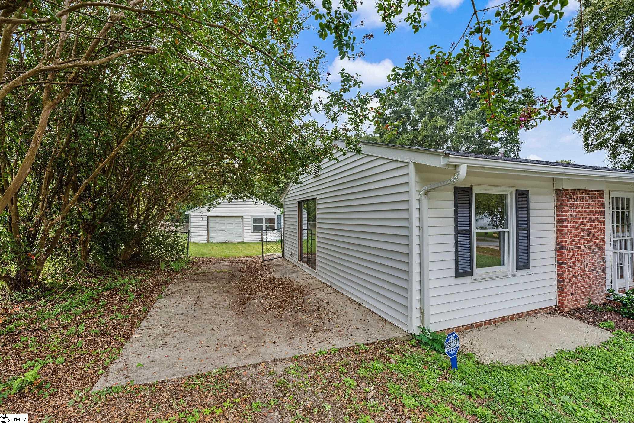 Single-story home with a concrete patio, mature trees, and a detached garage.