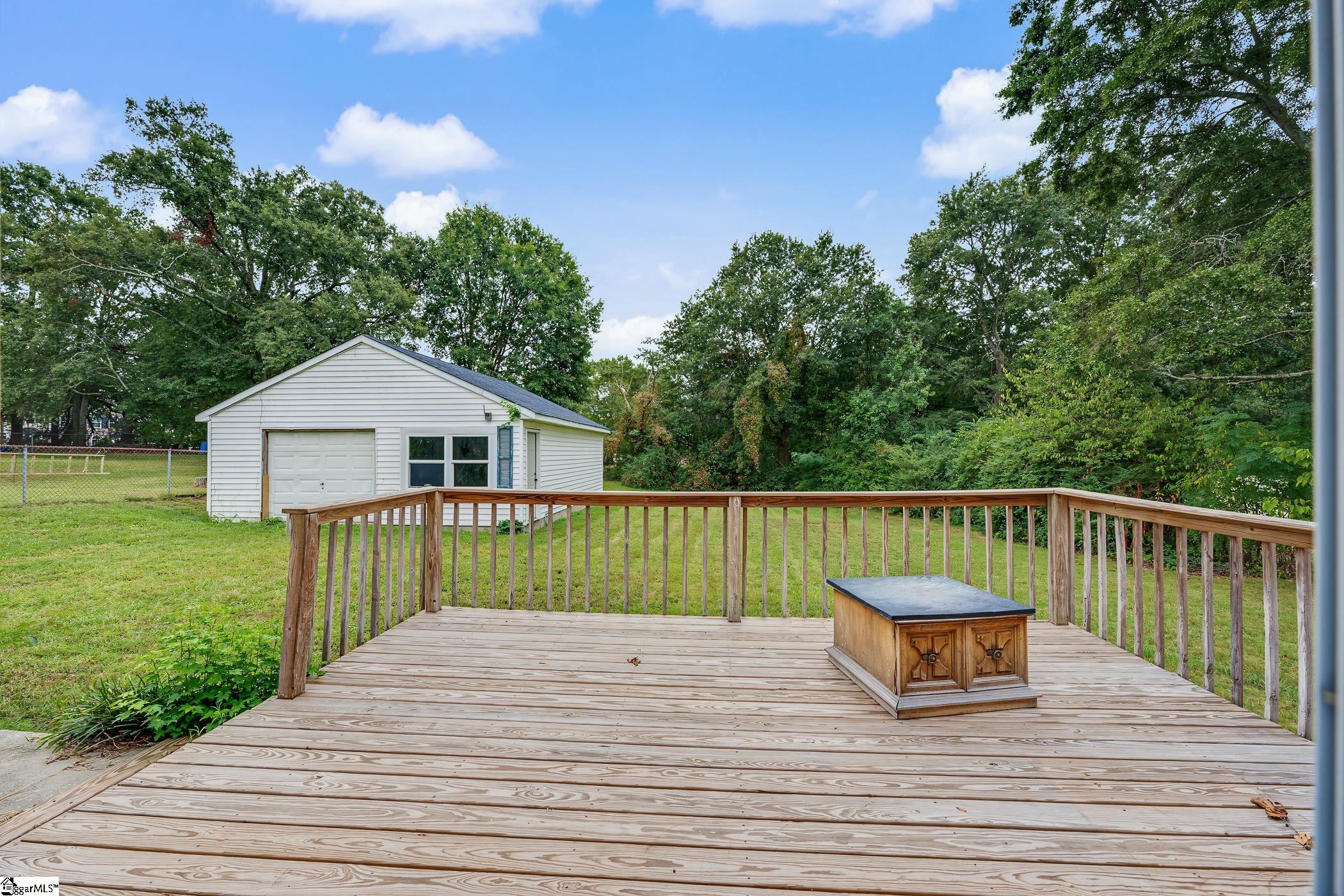 Backyard deck overlooking a grassy yard and detached white garage, with mature trees behind it.