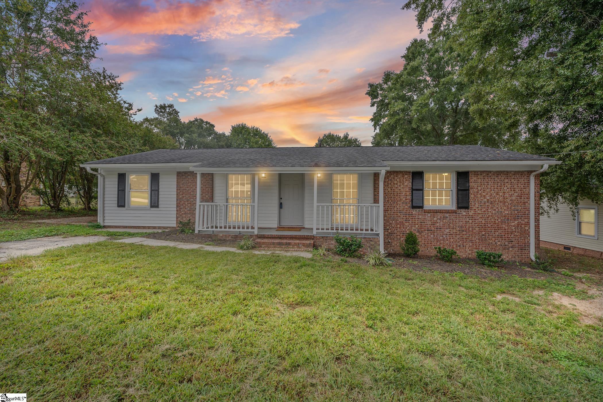 Single-story brick-and-siding ranch home with a covered front porch and broad lawn at sunset.