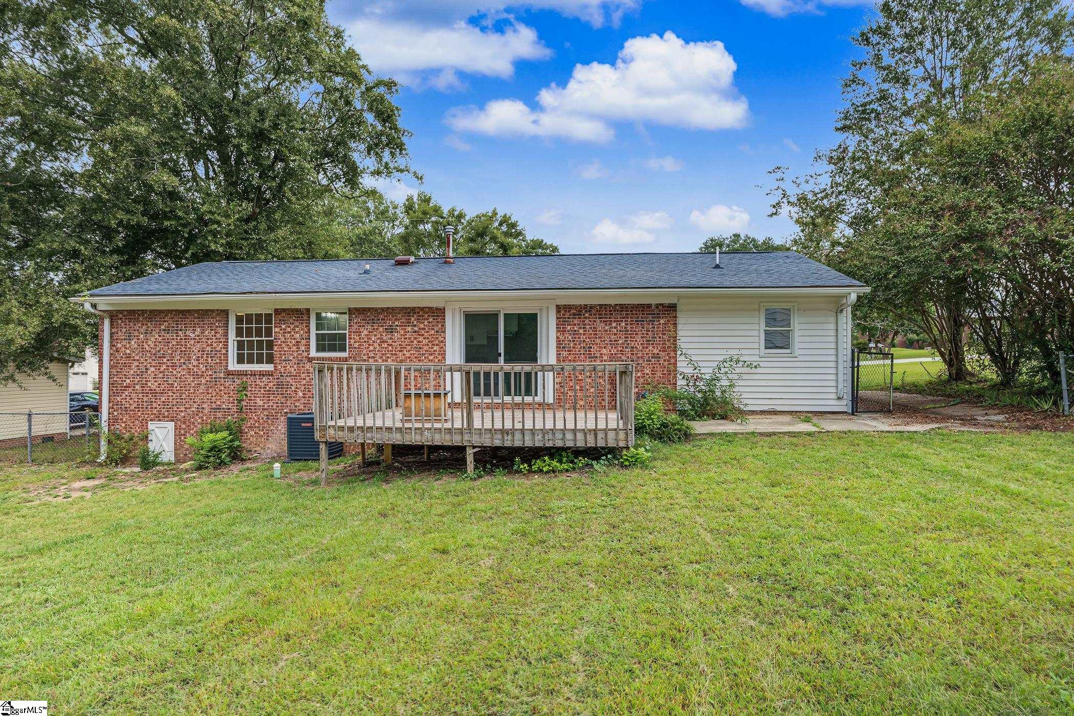 Rear of a brick house with a raised wooden deck and spacious grassy backyard.
