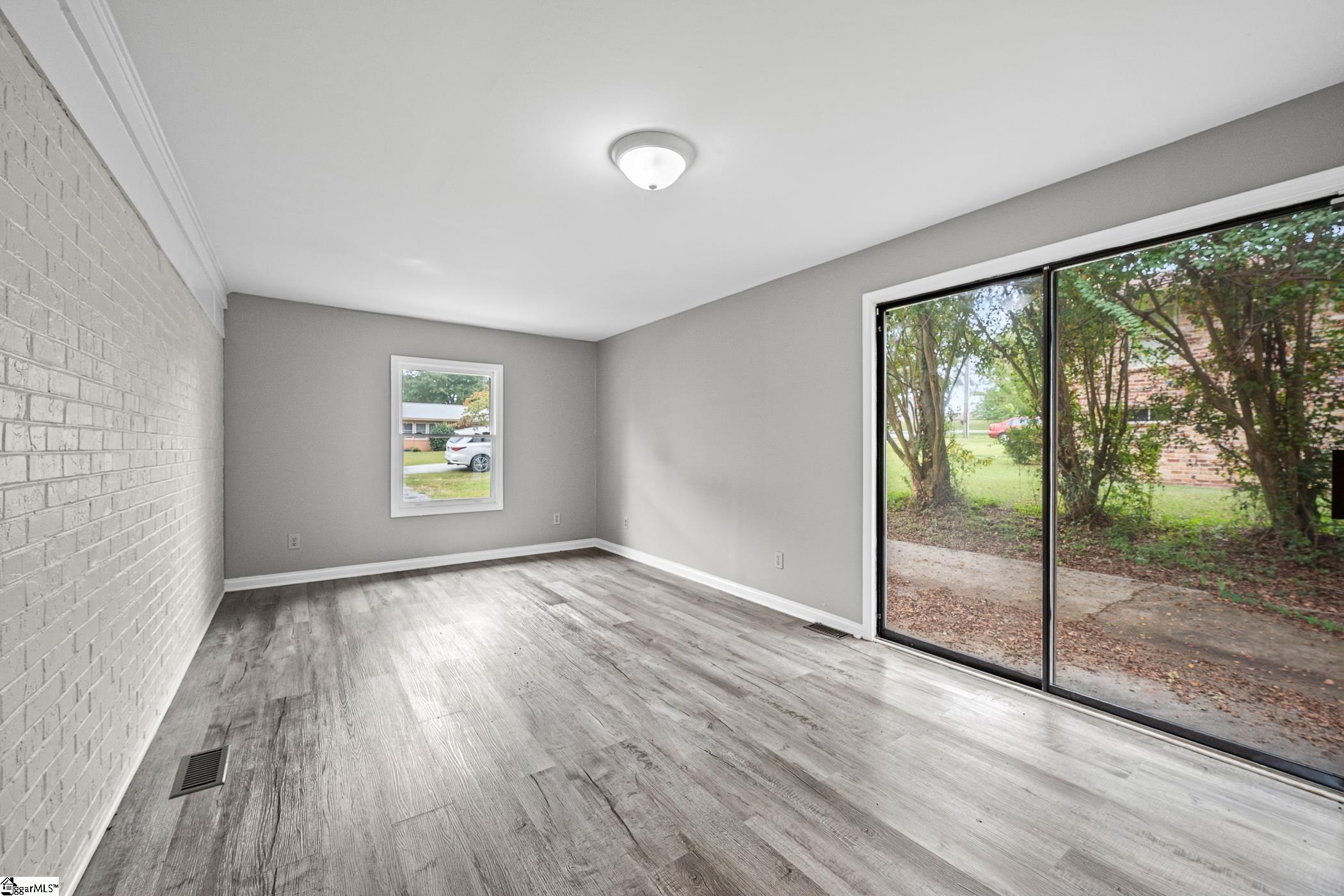 Vacant room with a white brick accent wall, gray flooring, and sliding glass doors to the yard.