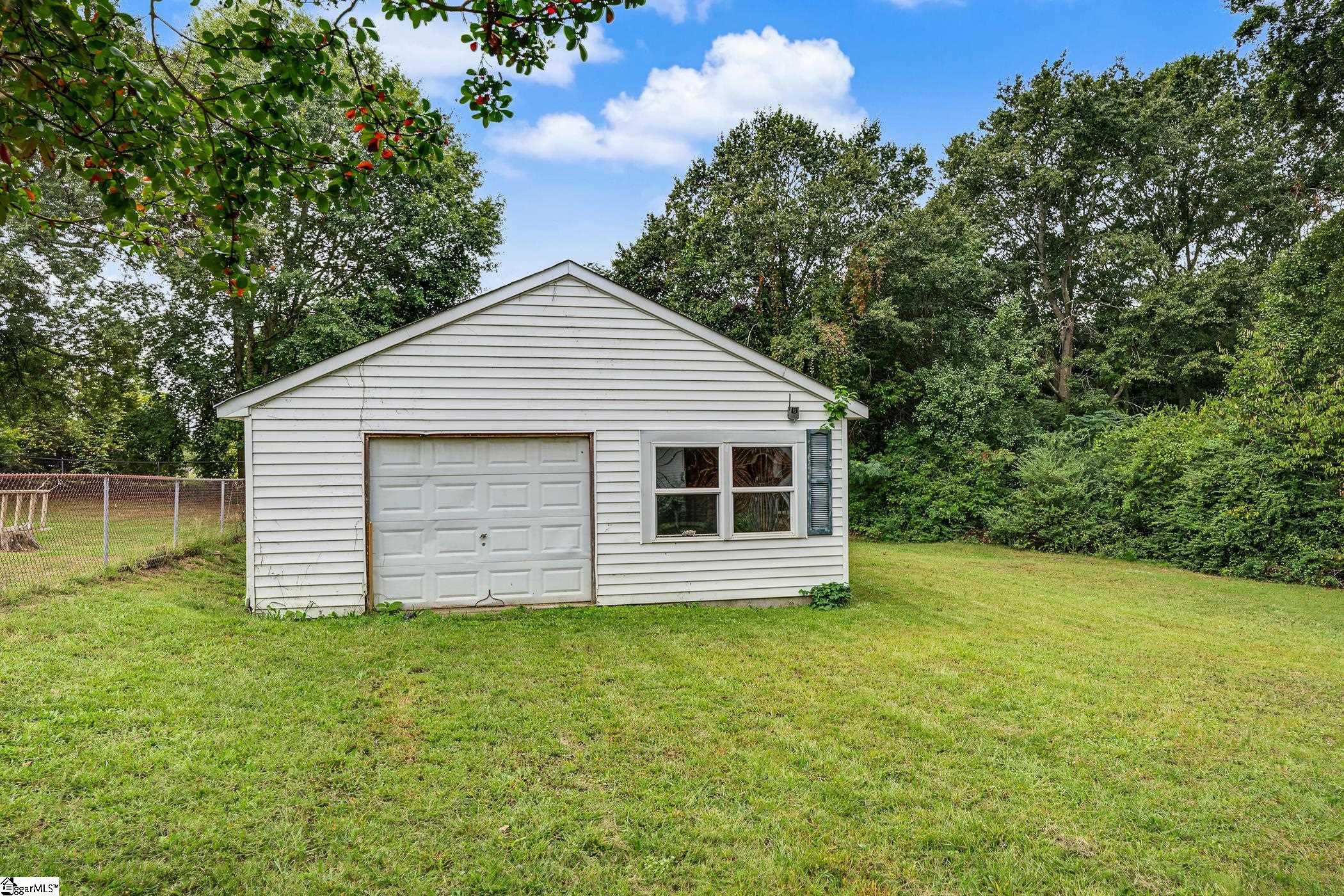 White detached garage with a paneled door and double window on a grassy lawn.