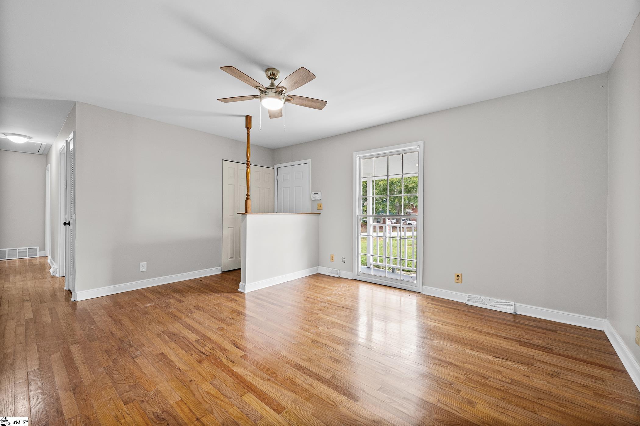 Empty room with hardwood floors, a ceiling fan, and a glass-paneled door to the porch.