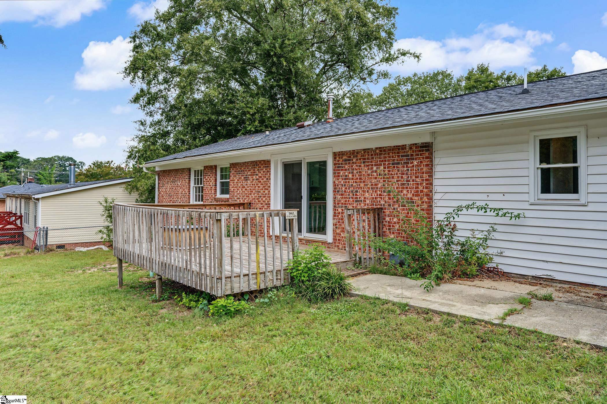 Rear of a brick-and-siding house with a raised wooden deck and grassy backyard.