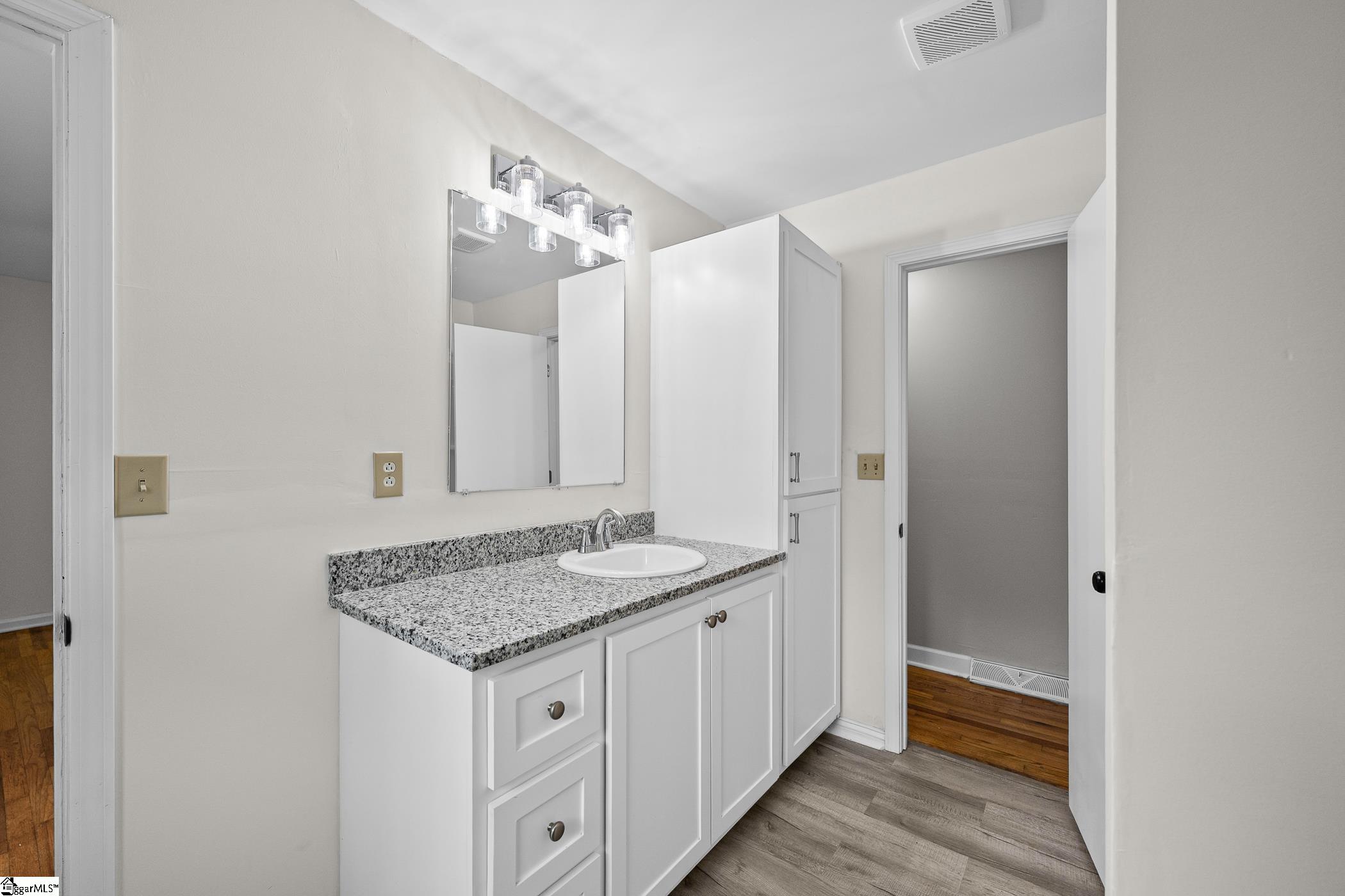 Bathroom vanity with speckled granite countertop, white cabinets, and mirrored medicine cabinet.