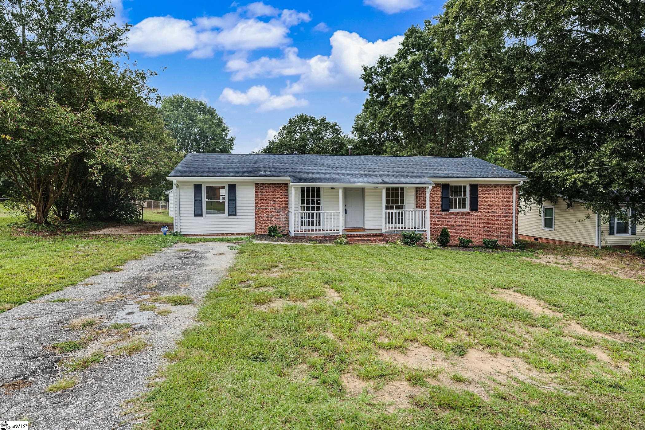 Single-story brick-and-siding ranch with a covered porch, broad grassy yard, and weathered driveway.