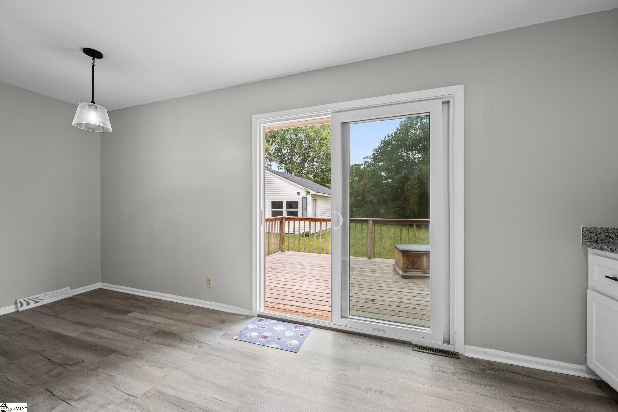 Empty dining area with gray walls and wood-look flooring, opening onto a raised deck through sliding glass doors.