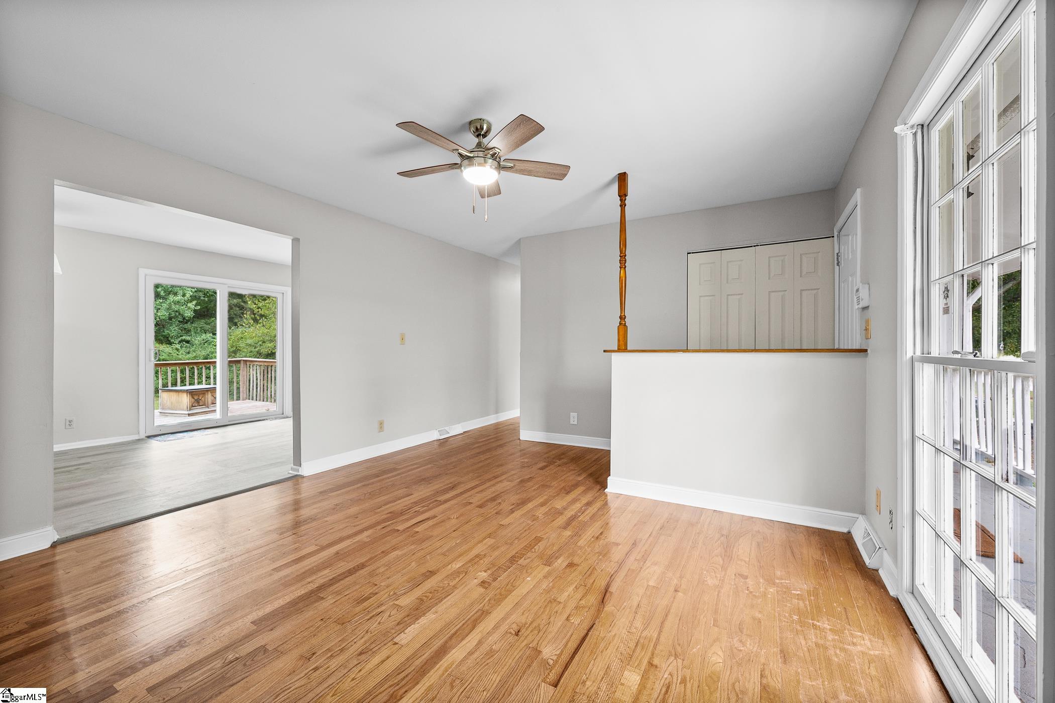 Vacant living room with hardwood floors, a raised breakfast bar, and large windows overlooking a deck.