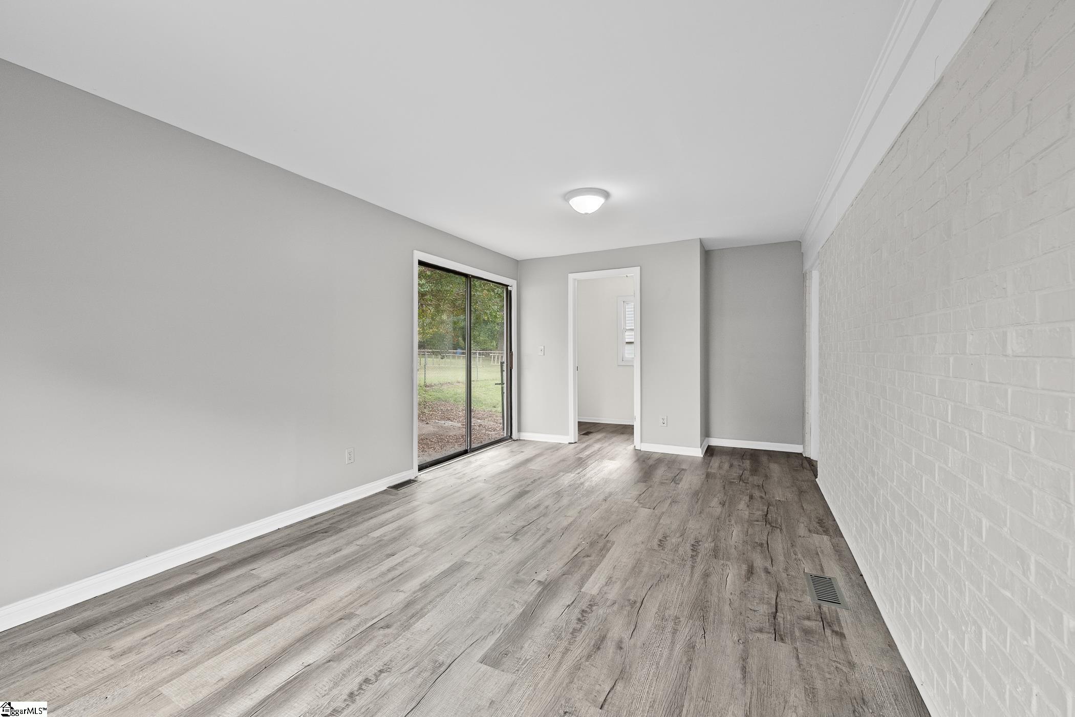 Unfurnished room with gray wood-look floors, a white brick wall, and sliding glass doors to the yard.
