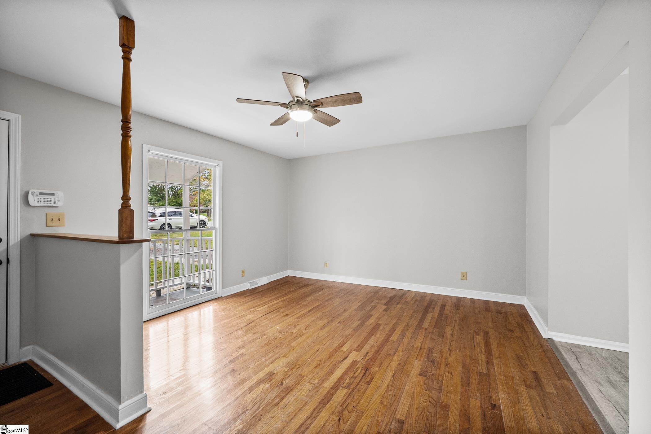 Vacant room with polished hardwood floors, a ceiling fan, and a tall divided-pane glass door.