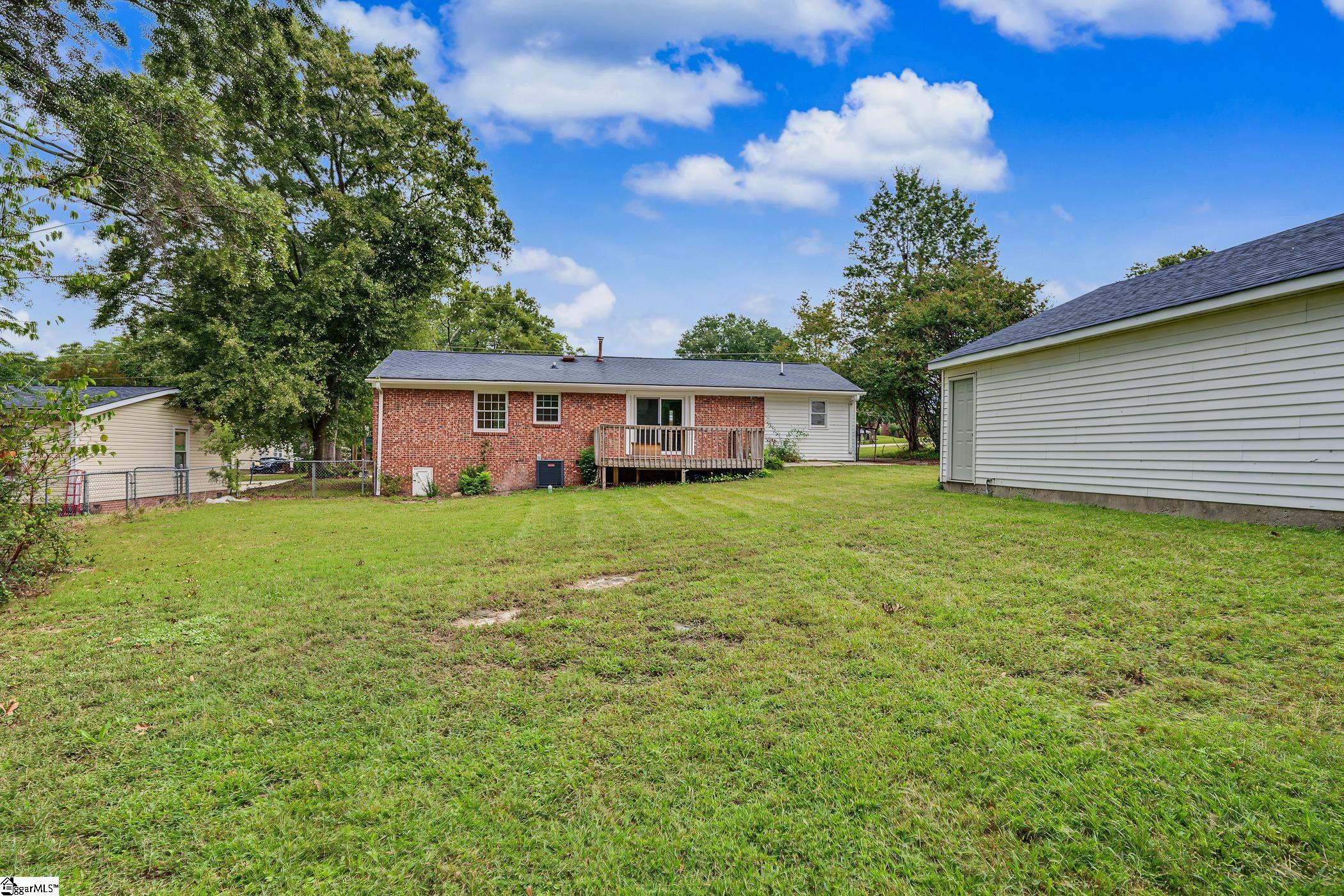 Rear of a brick-and-siding house with a small deck overlooking a broad grassy backyard.