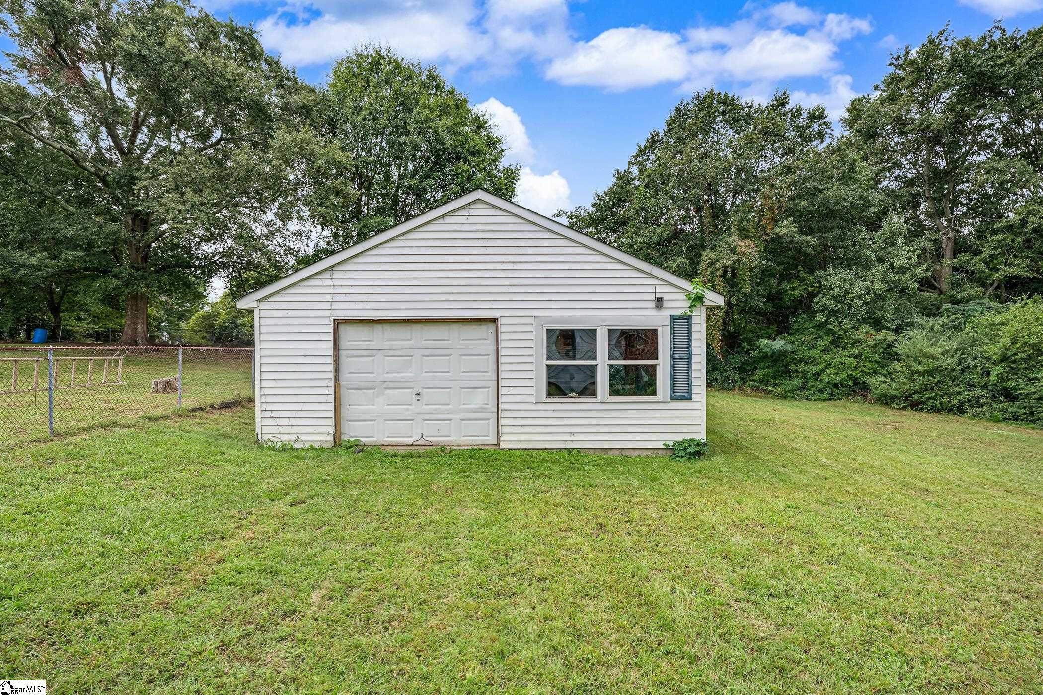 Detached white garage with an overhead door and front windows in a grassy, tree-lined yard.