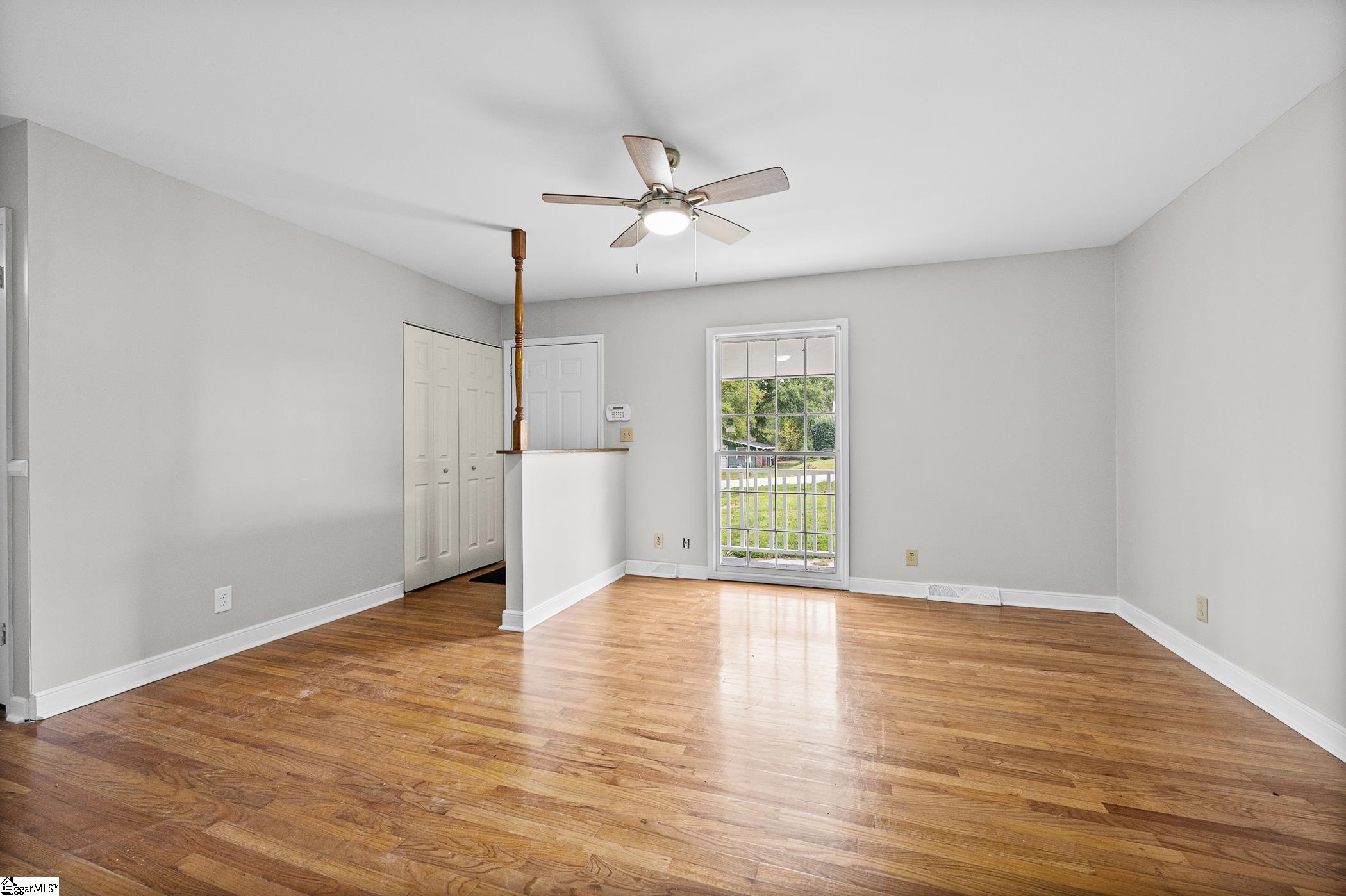 Empty room with polished hardwood floors, a ceiling fan, and a glass door overlooking the lawn.