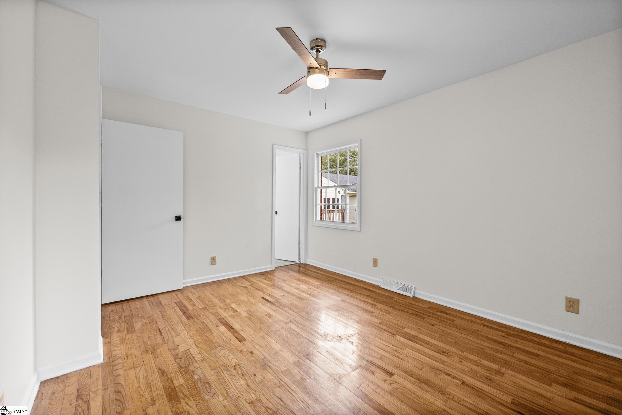 Empty bedroom with hardwood floors, a ceiling fan, and a window.