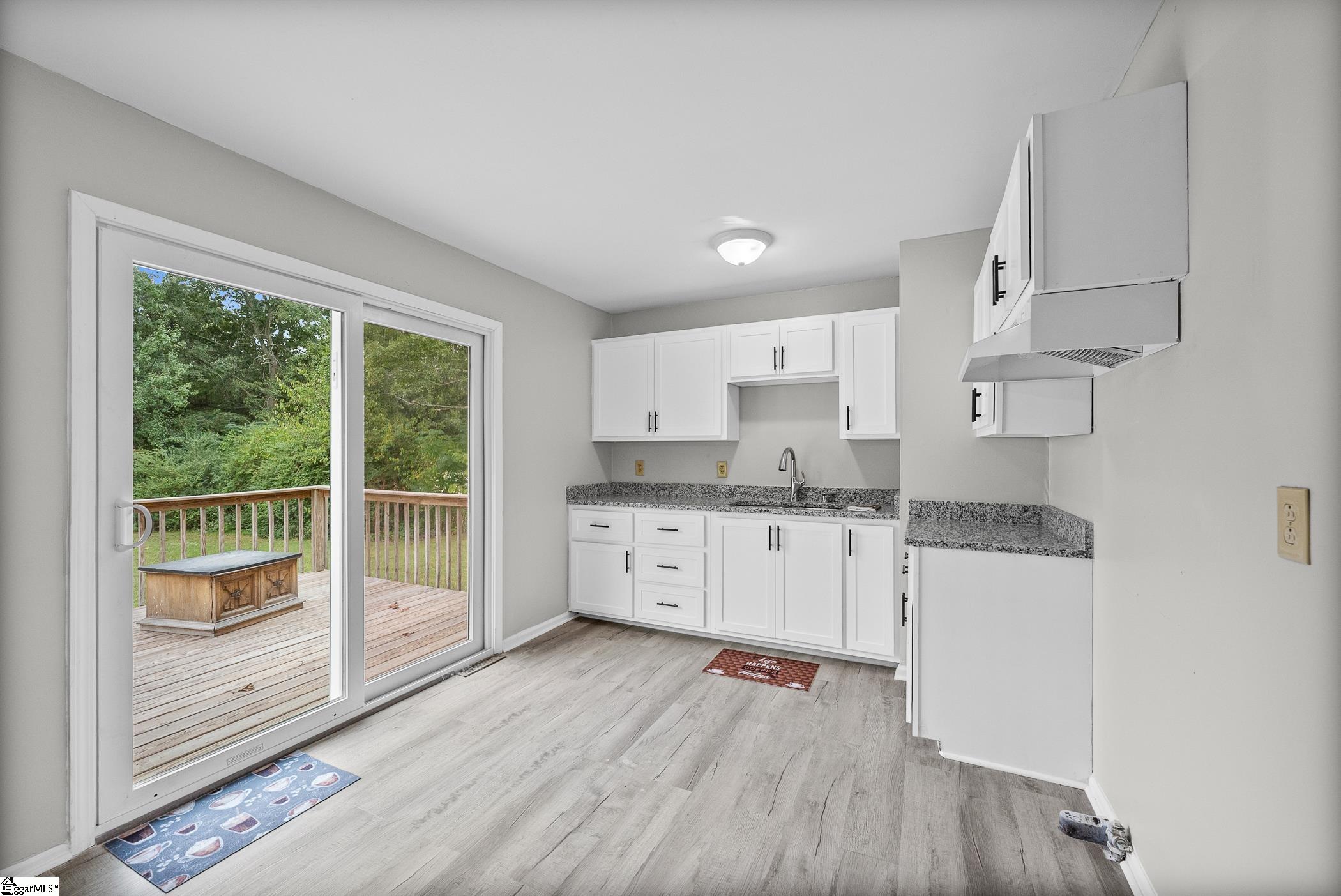 Bright kitchen with white cabinets and granite counters, opening onto a wooded deck.