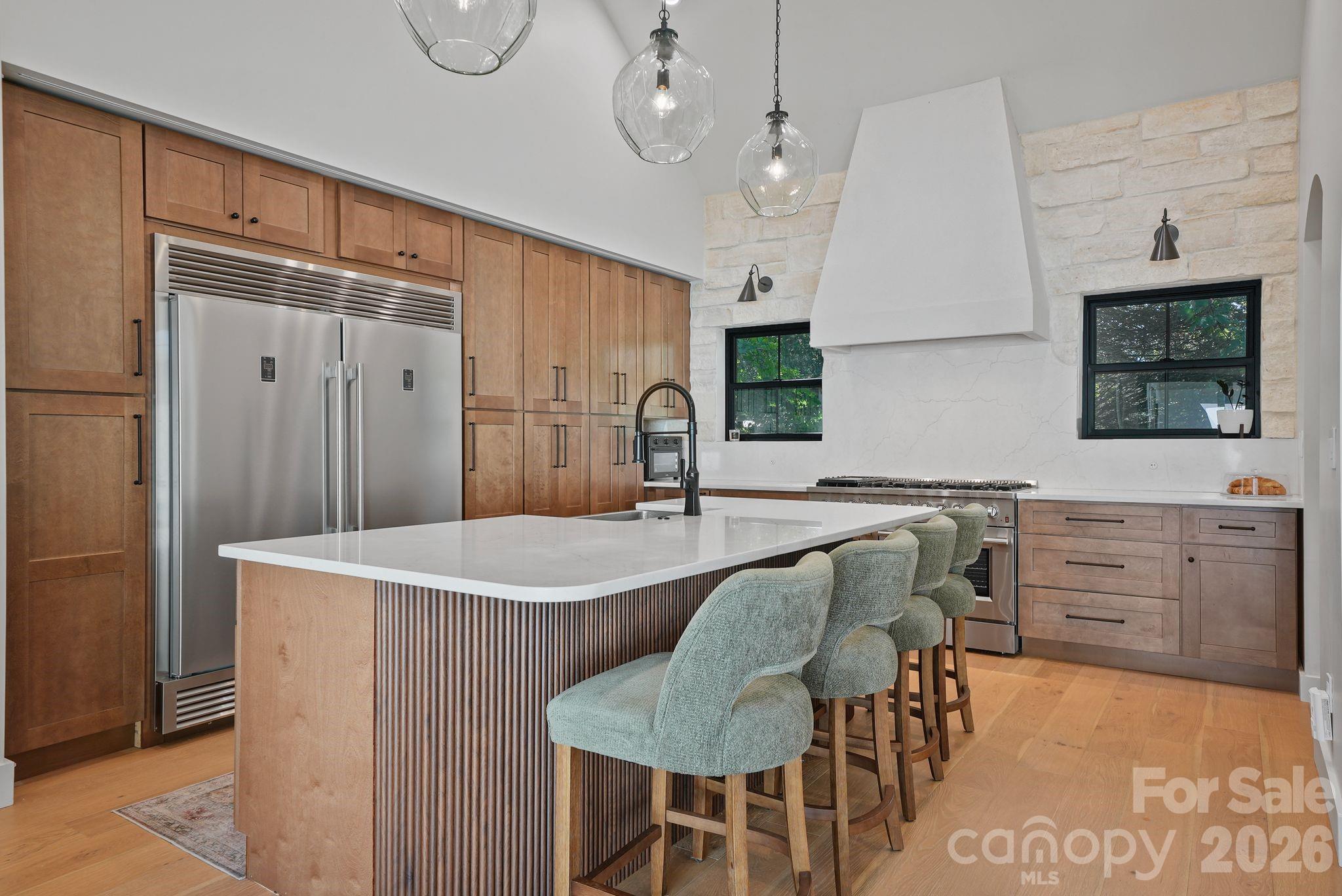 Modern kitchen with warm wood cabinets, a white island, and green upholstered stools.