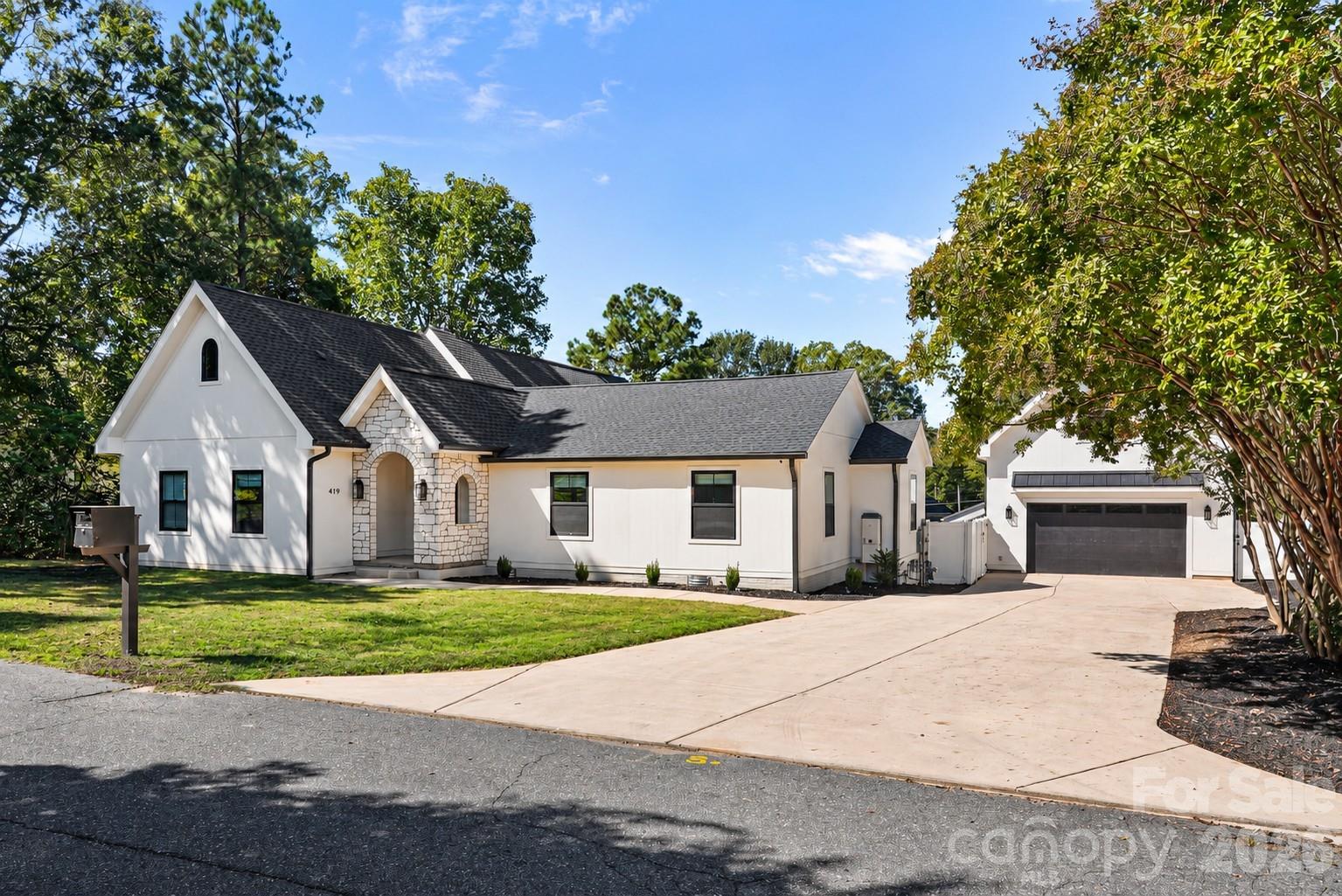 White house with stone arched entry and broad driveway leading to a detached garage.