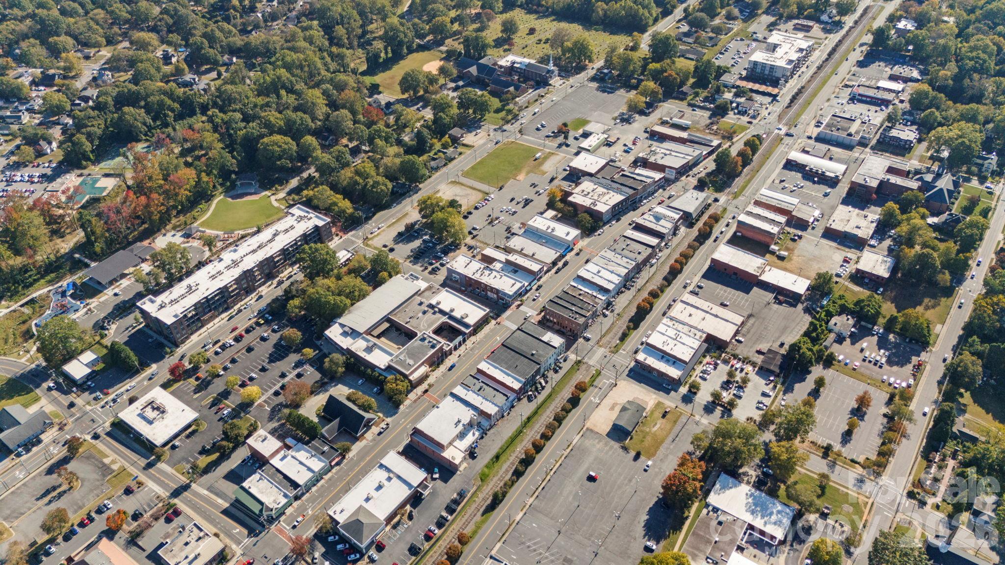 Aerial view of a town center with a tree-lined park, playground, and rows of commercial buildings.