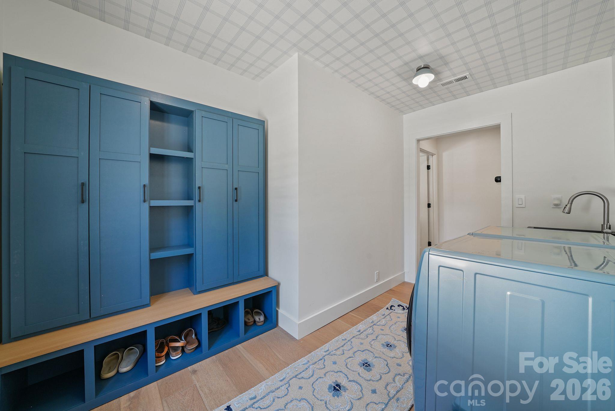Mudroom with blue built-in storage, shoe cubbies, a wood bench, and a large utility sink.