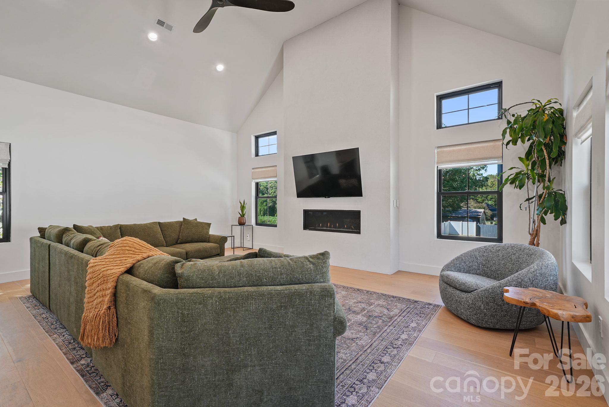 Vaulted living room with a green sectional, wall-mounted TV, linear fireplace, and large windows.