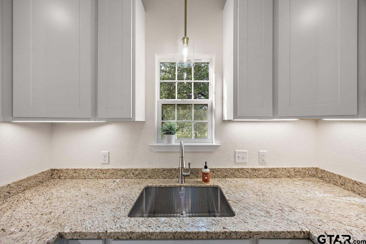Bright kitchen with granite countertops, an undermount sink, white cabinets, and a window.