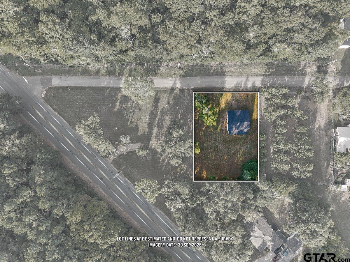 Aerial view of a wooded property with the house outlined beside a paved road.