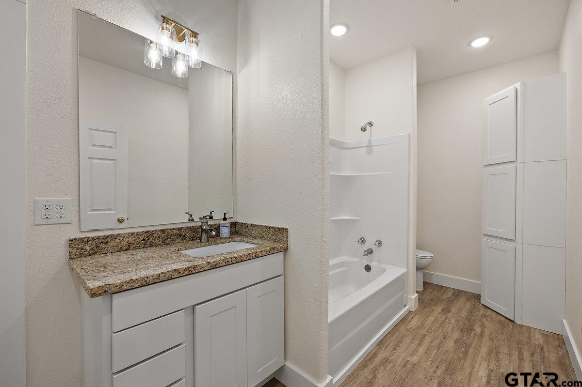 Bathroom with a granite vanity, bathtub and shower, and tall white storage cabinets.