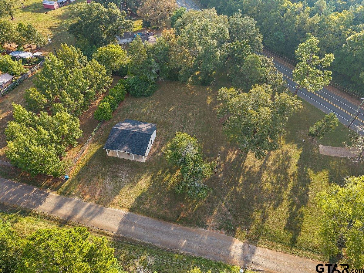 Aerial view of a wooded lot with a small white building beside a paved road.