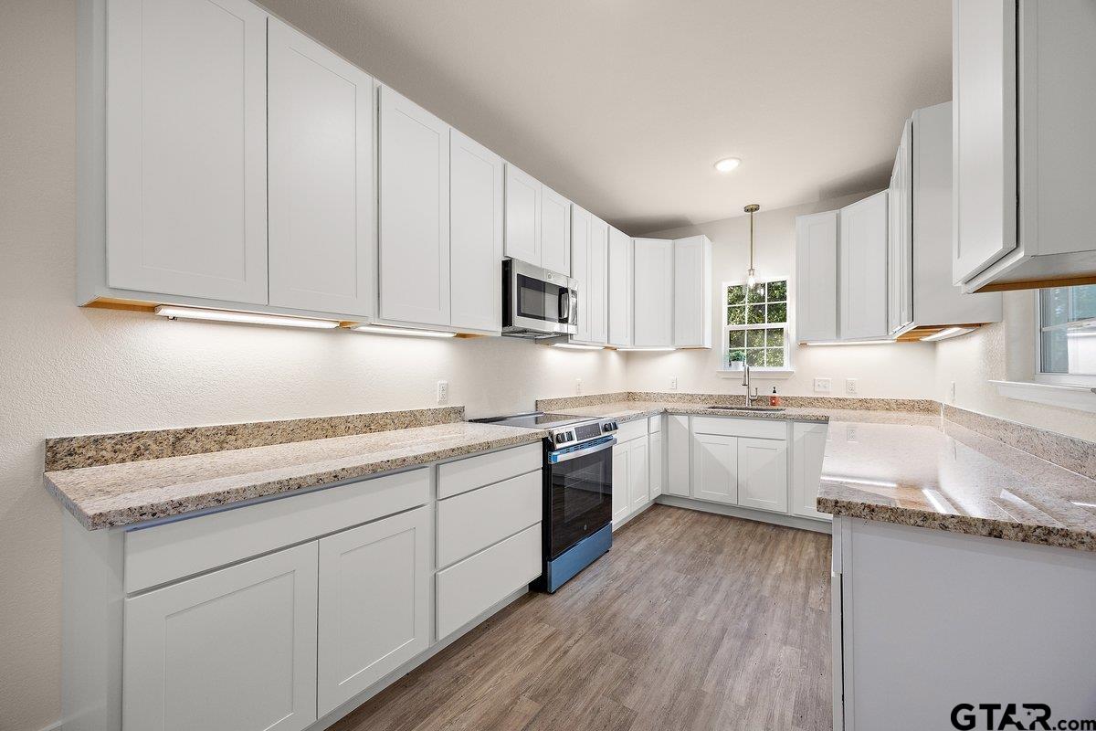 Kitchen with white cabinets, speckled stone counters, stainless steel appliances, and wood-look flooring.