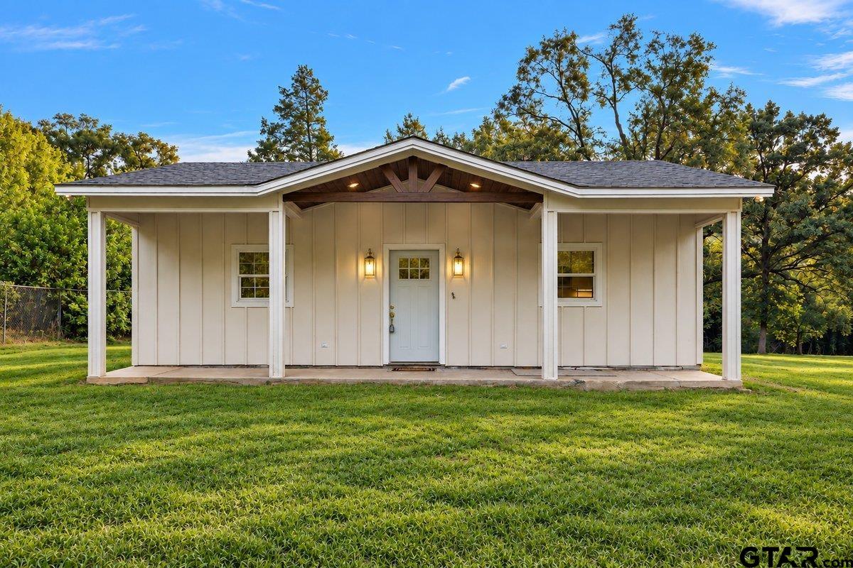 Single-story home with a covered gabled porch, pale siding, and a broad green lawn.