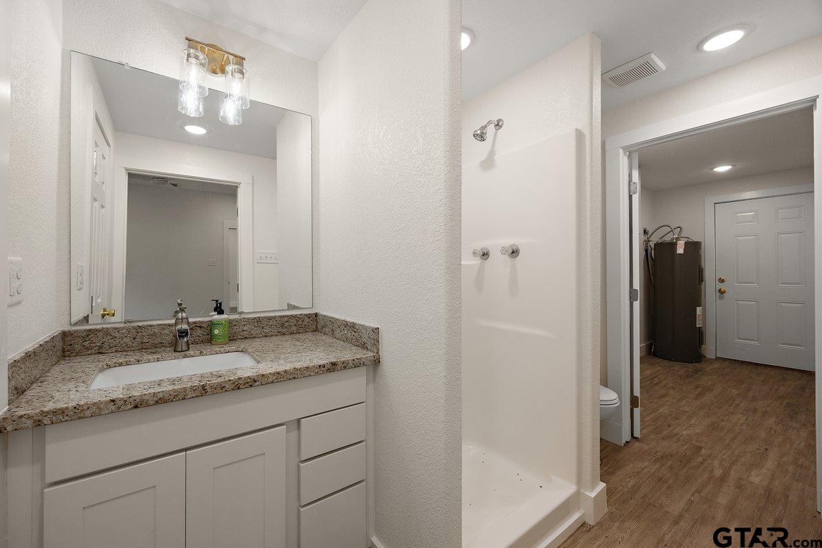 Bathroom with a white vanity and walk-in shower; doorway opens to a room with a water heater.