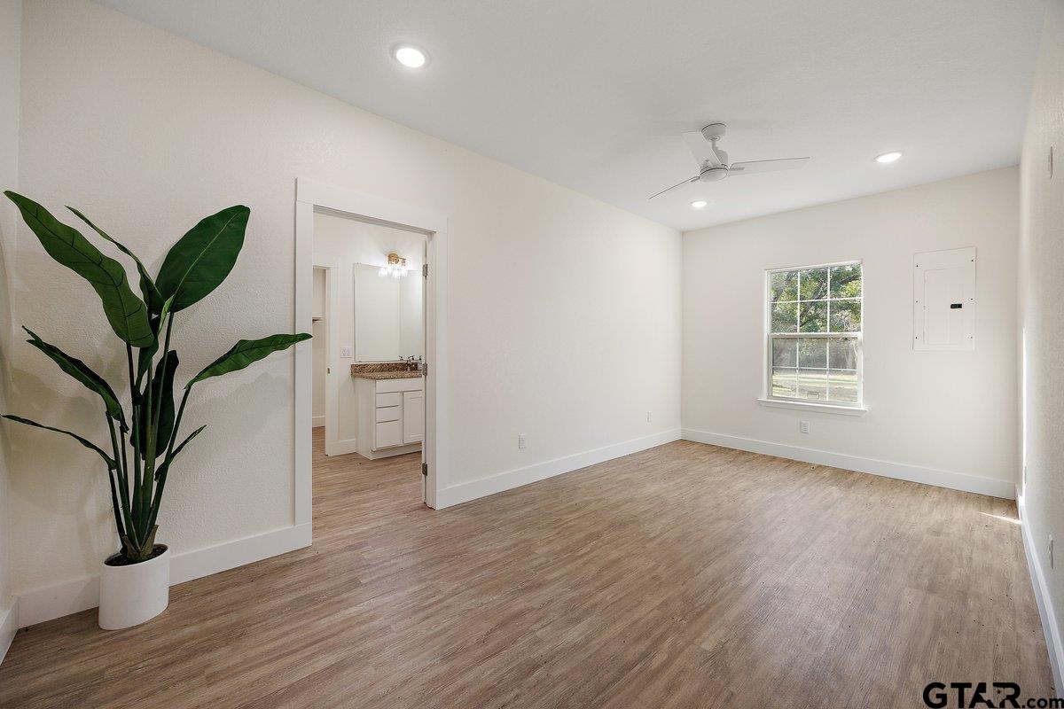 Vacant room with wood-look flooring, a ceiling fan, and a doorway to a bathroom vanity.